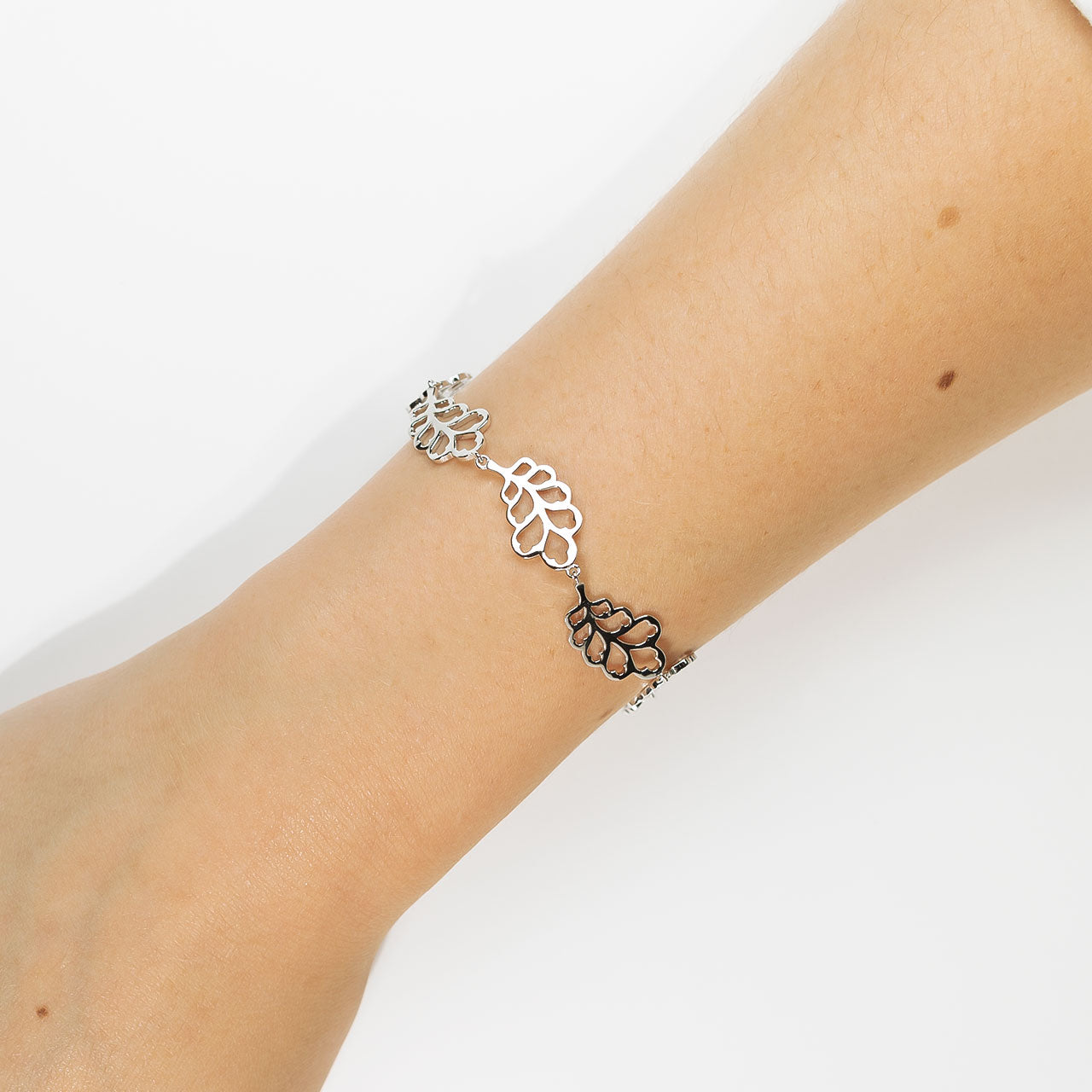 Delicate sterling silver bracelet featuring linked oak leaf motifs with an extension chain, styled simply on the wrist against a white background.