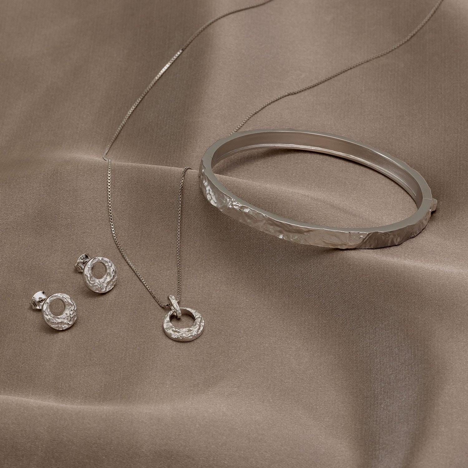 Silver jewelry set including a necklace, bracelet, and earrings on a brown fabric background