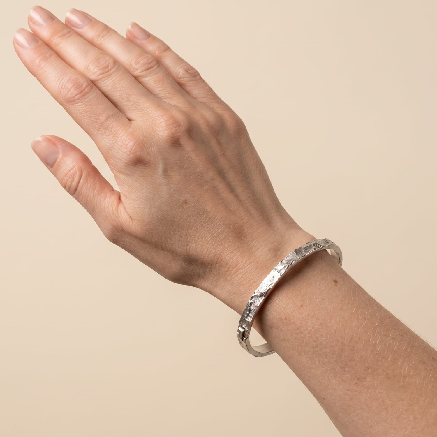 Model wears sterling silver bangle featuring a sculpted textured band with a polished interior and secure clasp.