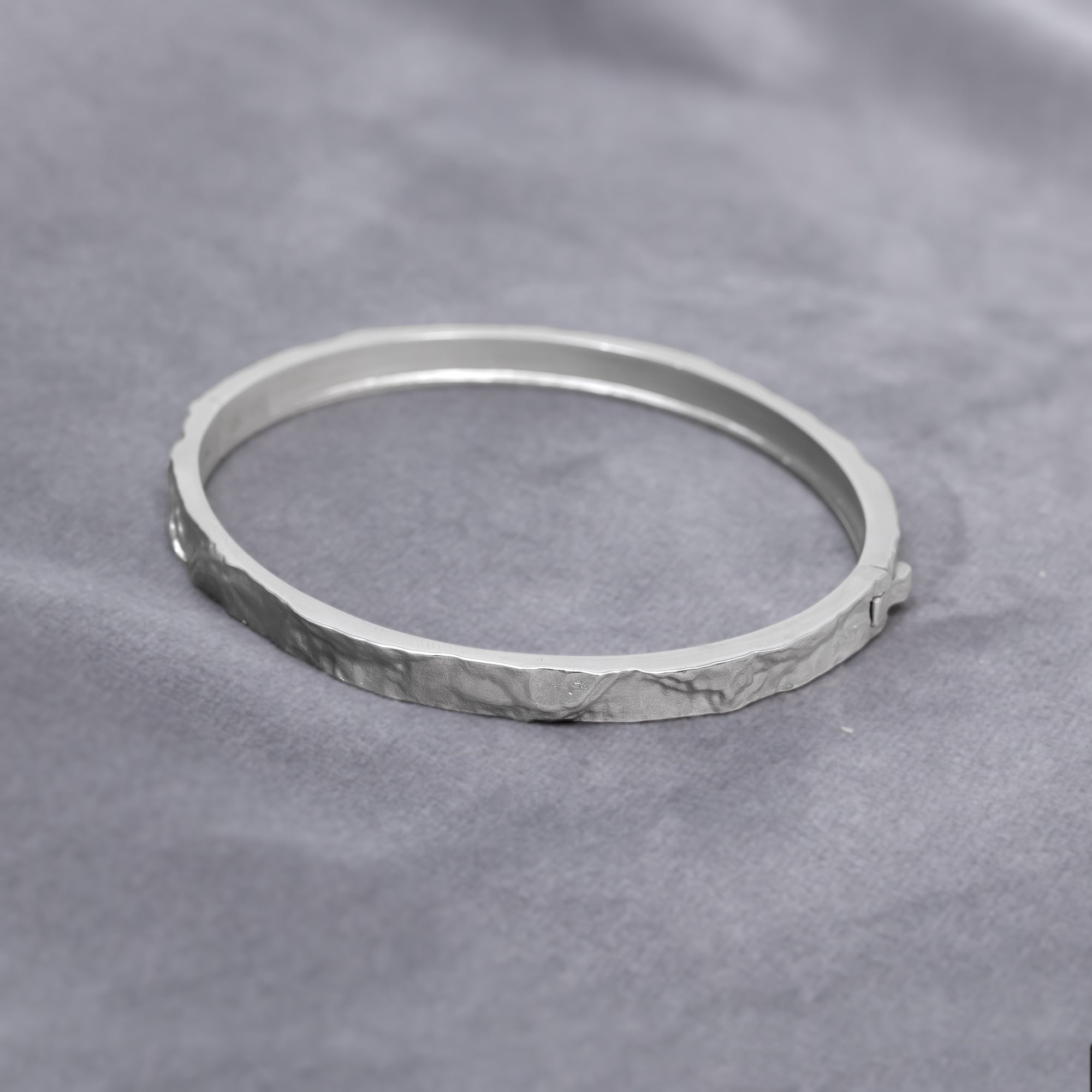 Sterling silver bangle featuring a sculpted textured band with a polished interior and secure clasp, showcasing contemporary British silver jewellery craftsmanship by Azendi. Placed on a grey velvet cloth.