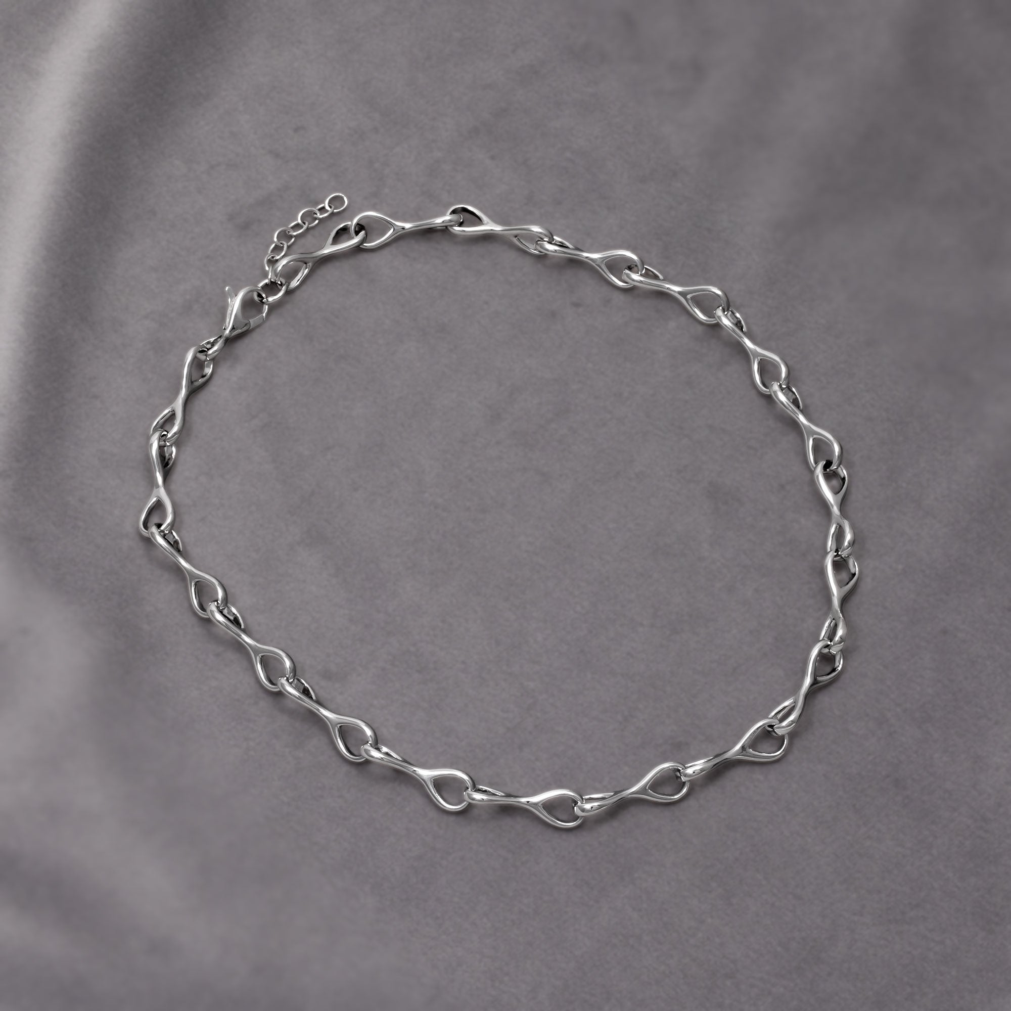 Necklace featuring interlocking teardrop links with smooth, flowing contours for a modern, sculptural expression in silver jewellery. Placed on a grey velvet cloth.