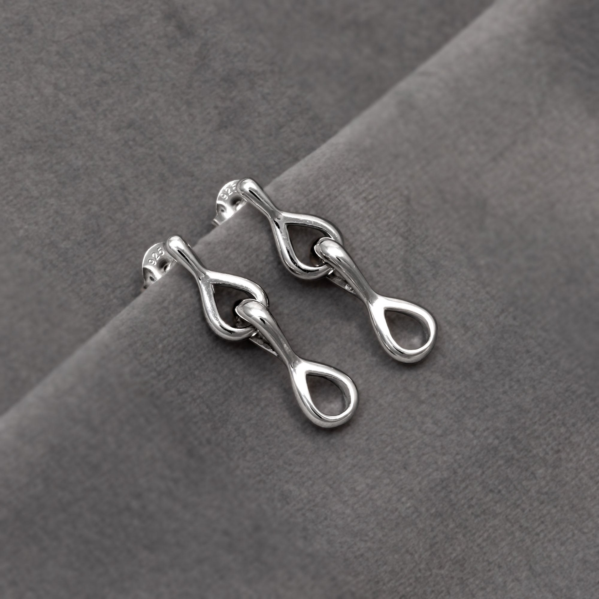 Drop earrings featuring interlocking teardrop links with smooth, flowing contours for a modern, sculptural expression in silver jewellery. Placed on a grey velvet cloth.