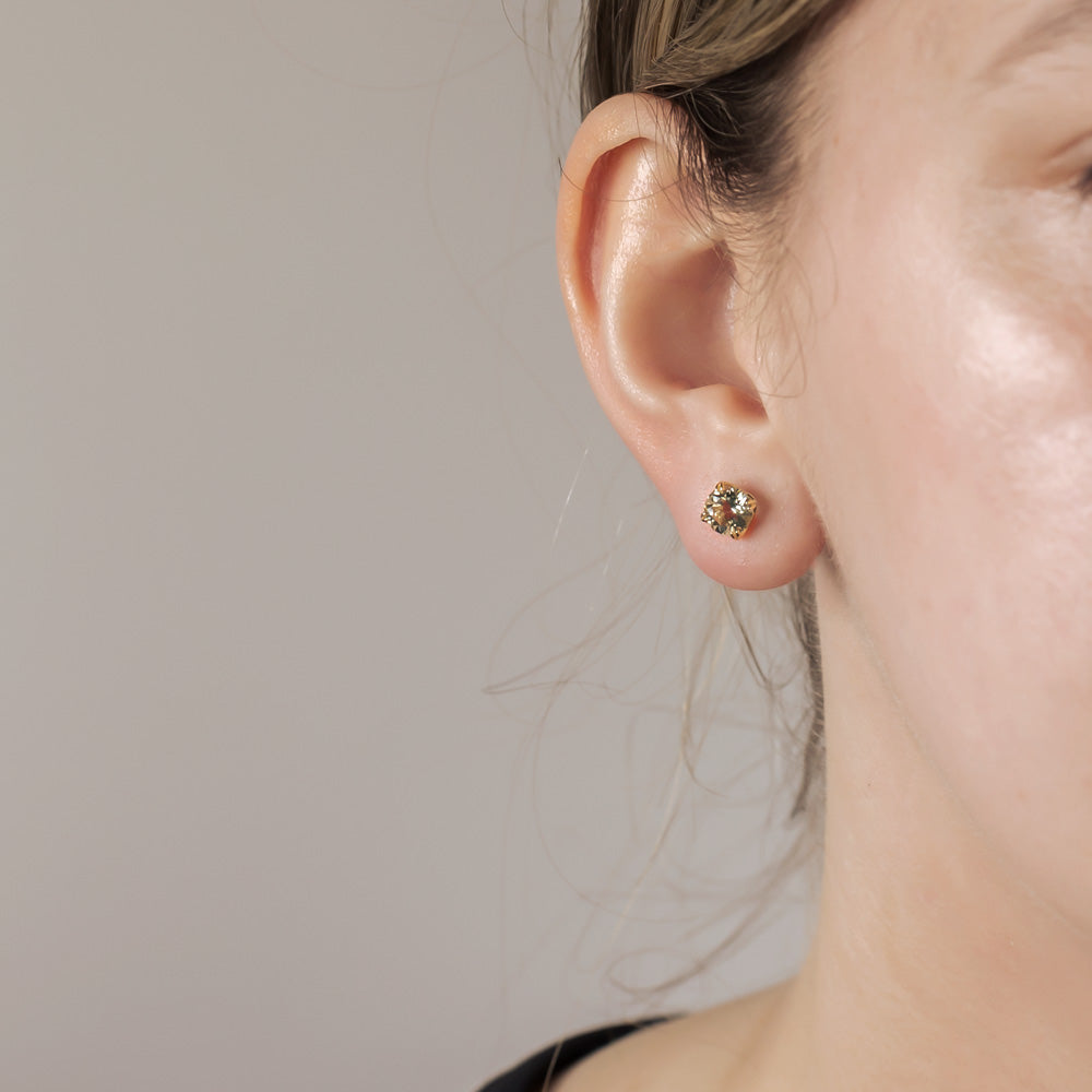 Close-up of an ear adorned with a 9 carat gold earring featuring a green amethyst solitaire in a minimalist, elegant design.