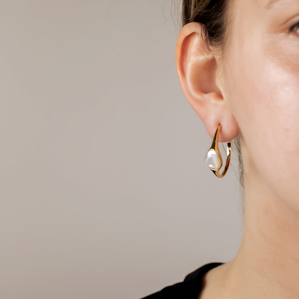 Close-up of a woman's ear wearing a gold vermeil hoop earring featuring a sculptural design with a polished mother of pearl gem, highlighting elegant contemporary silver jewellery.