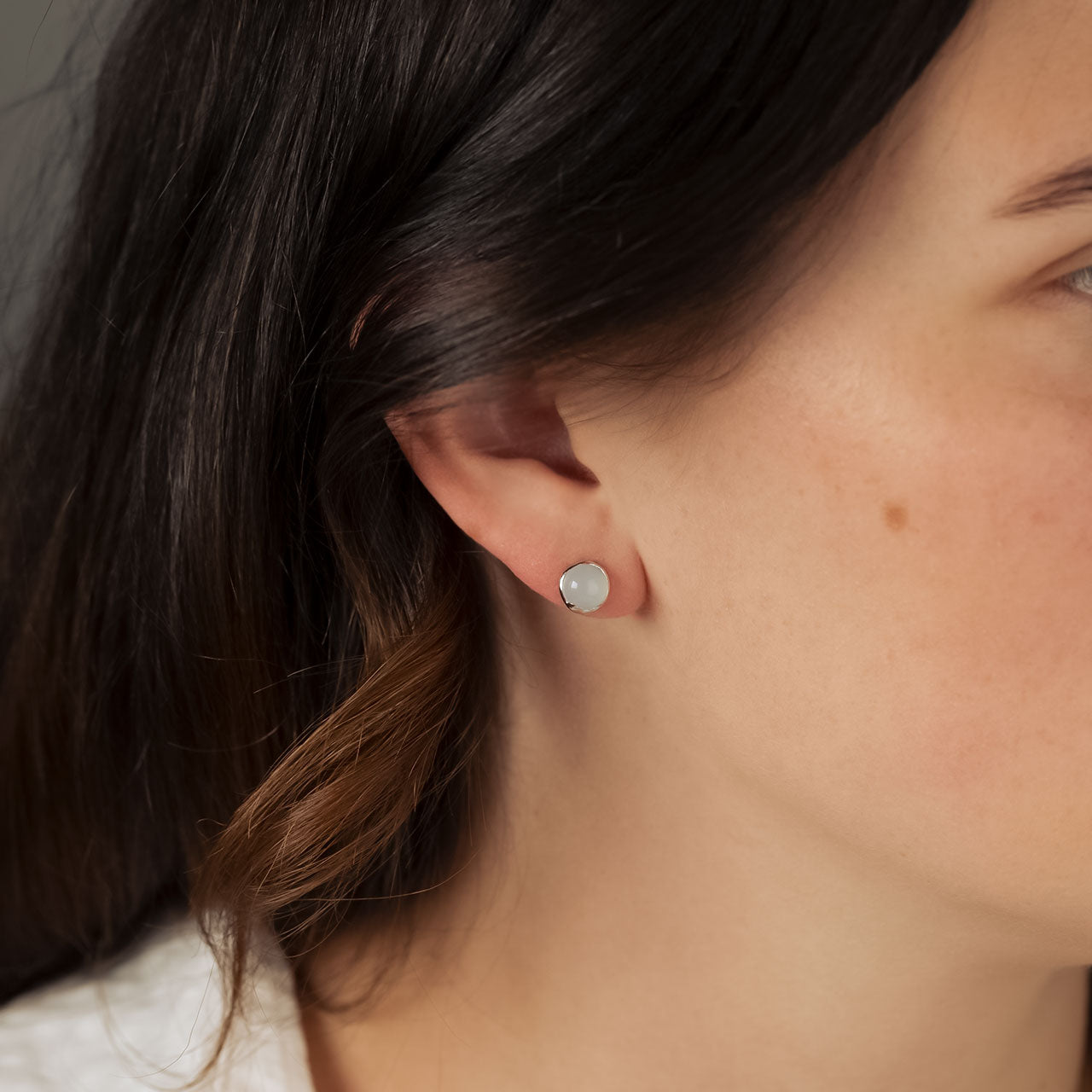 Close-up of an ear wearing a silver stud earring featuring a smooth rainbow moonstone in a polished bezel setting, highlighting contemporary sterling silver jewellery design.