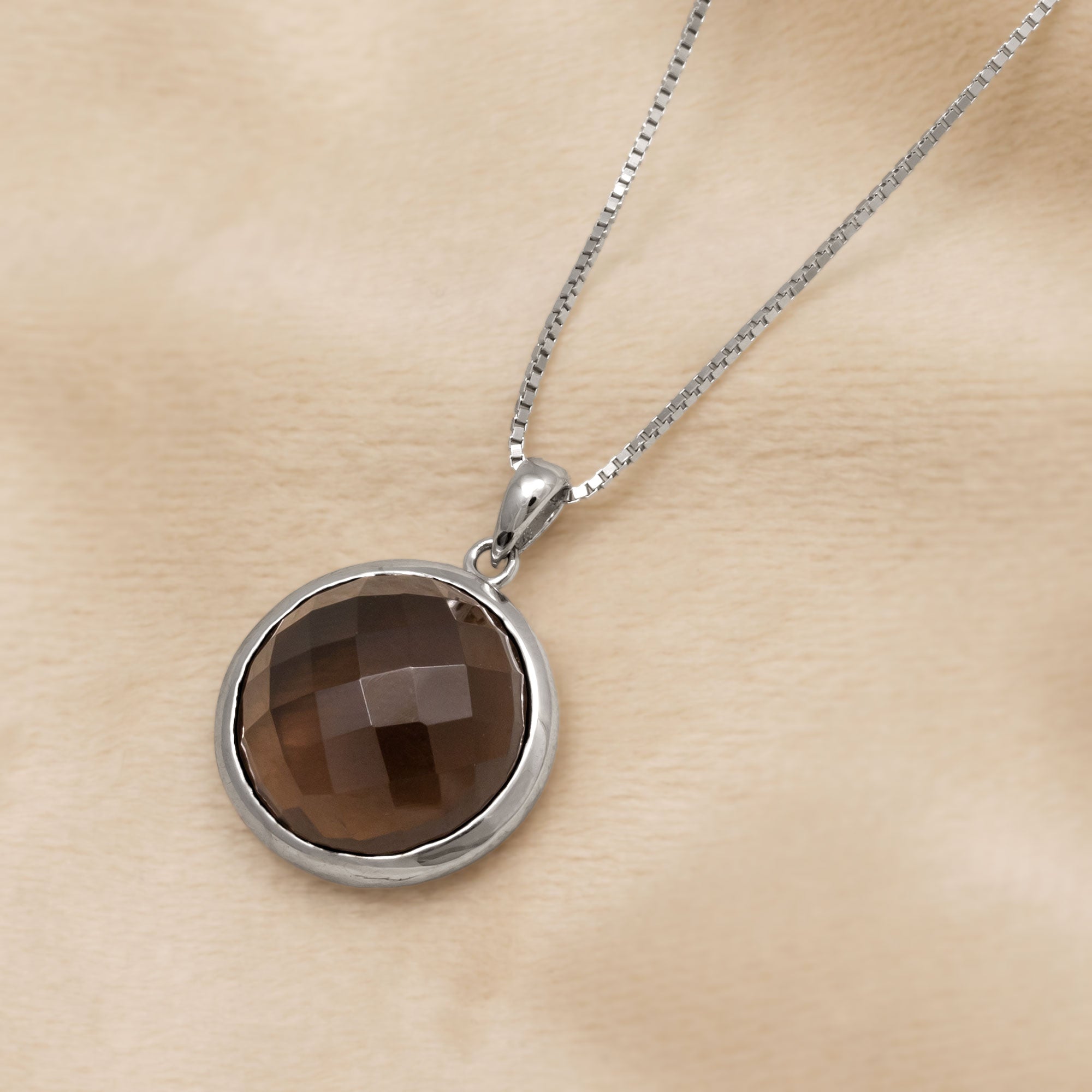 Sterling silver necklace featuring a checker-cut smoky quartz pendant with a polished bezel setting, displayed against a clean white background. Placed on a cream velvet cloth.