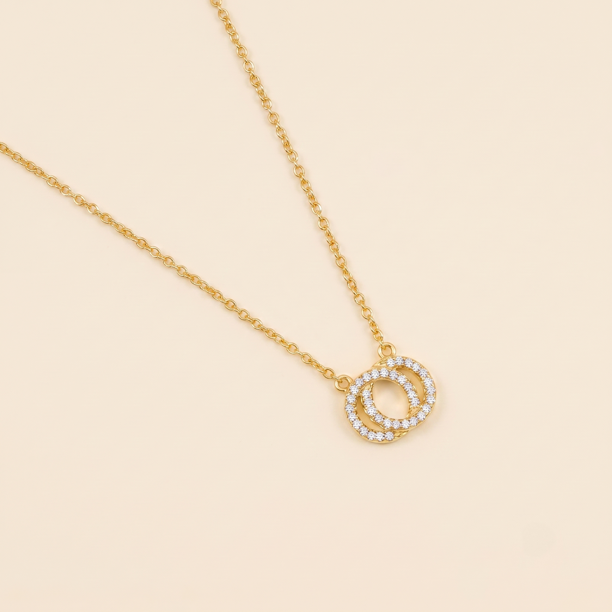 Delicate yellow gold vermeil necklace featuring two reversible interlocking circles embellished with sparkling stones, displayed on a plain cream background.