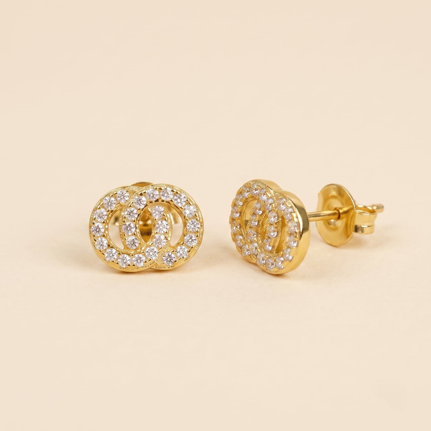 Pair of yellow gold vermeil stud earrings featuring interlocking circles paved with sparkling cubic zirconia, displayed on a plain cream background.