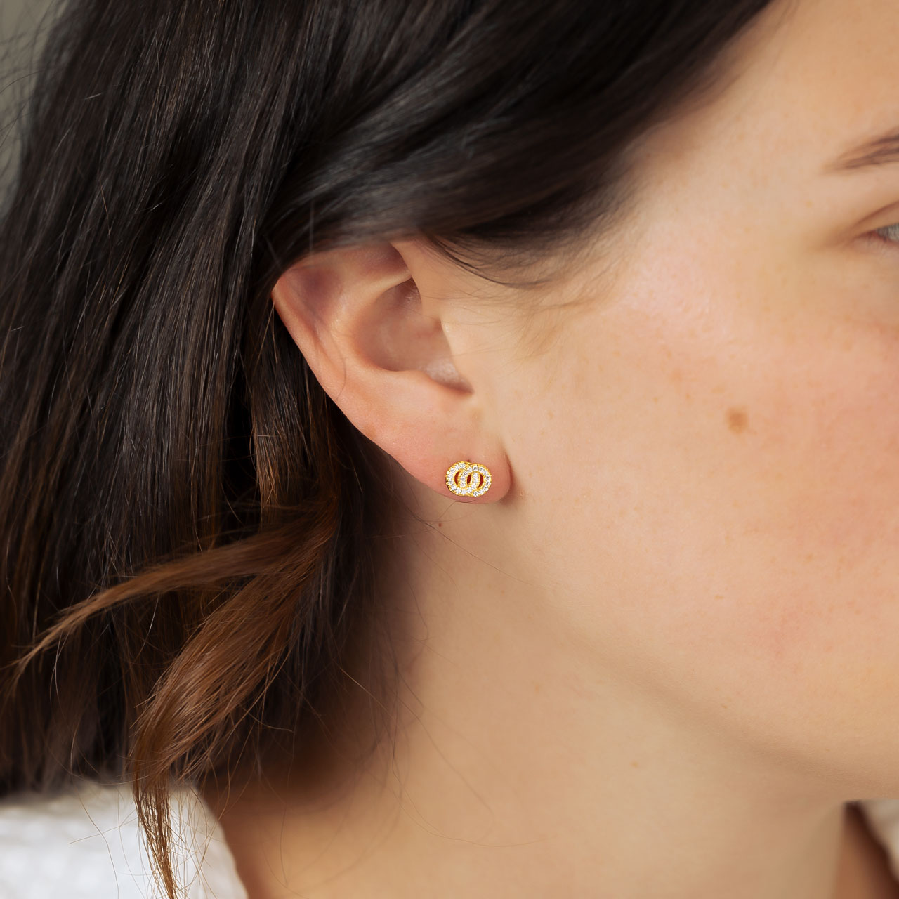 Pair of yellow gold vermeil stud earrings featuring interlocking circles accented with sparkling cubic zirconia, styled on the ear for a refined and elegant look.