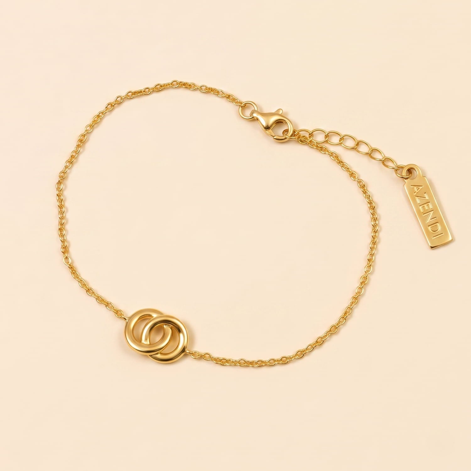 Delicate gold vermeil bracelet featuring two interlocking circles on a fine adjustable chain, laying on a cream background with a branded charm near the clasp.