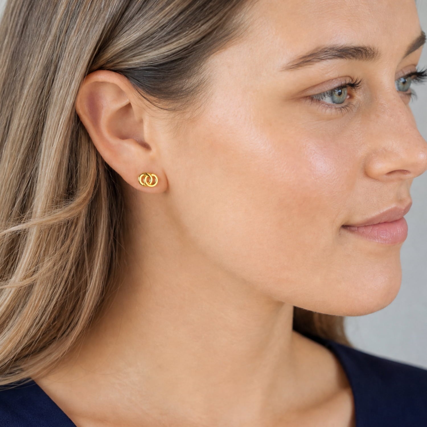 A pair of yellow gold vermeil stud earrings featuring an interlocking loop design, styled on a model’s ear to highlight their elegant and modern appeal.