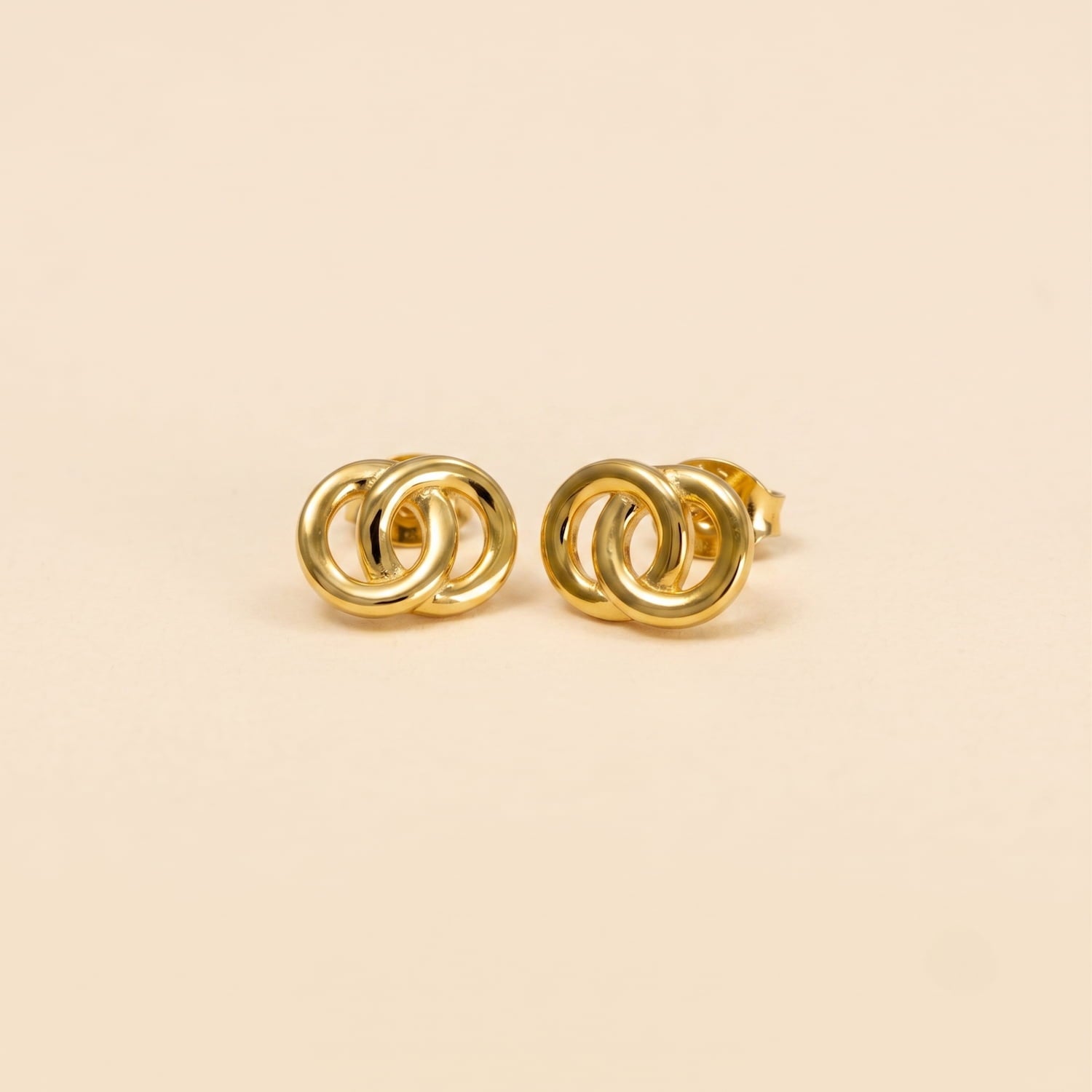 Pair of yellow gold vermeil stud earrings featuring a sculptural interlocking circular design, presented on a plain cream background.
