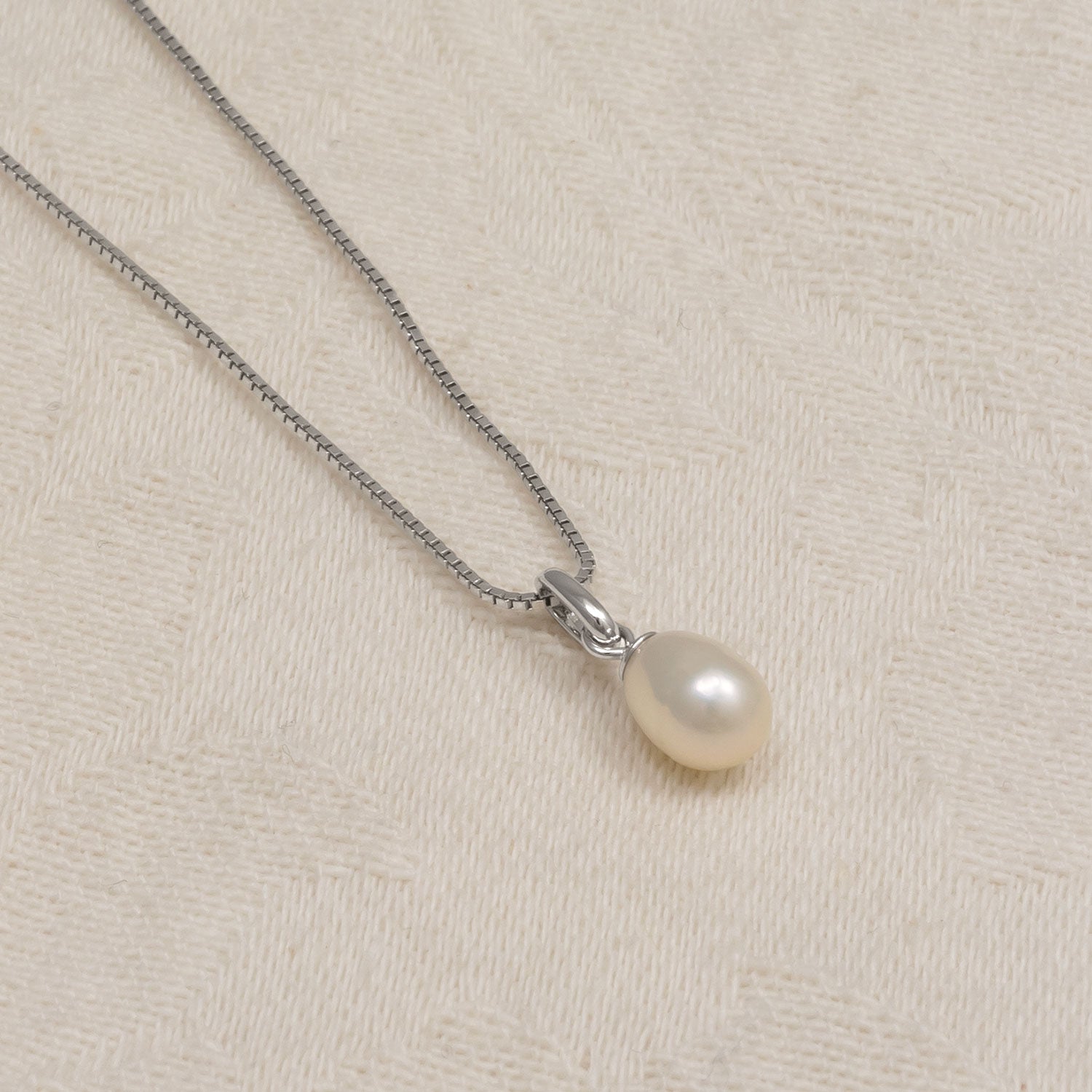 Delicate sterling silver necklace featuring a lustrous teardrop freshwater pearl pendant, displayed on a textured neutral fabric background.
