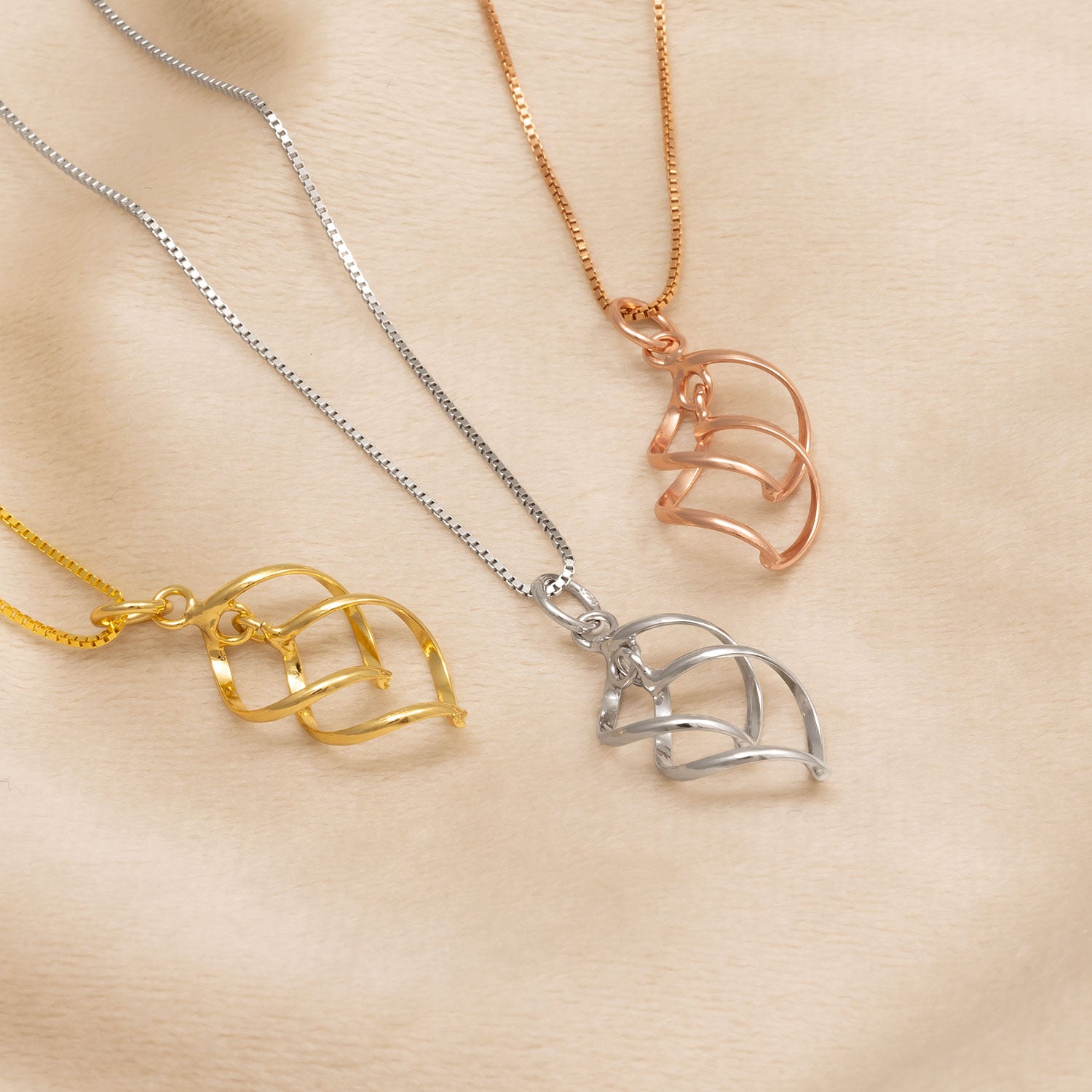 Three sculptural pendant necklaces in yellow gold vermeil, sterling silver, and rose gold vermeil, featuring an elegant wave-inspired openwork design on delicate chains.