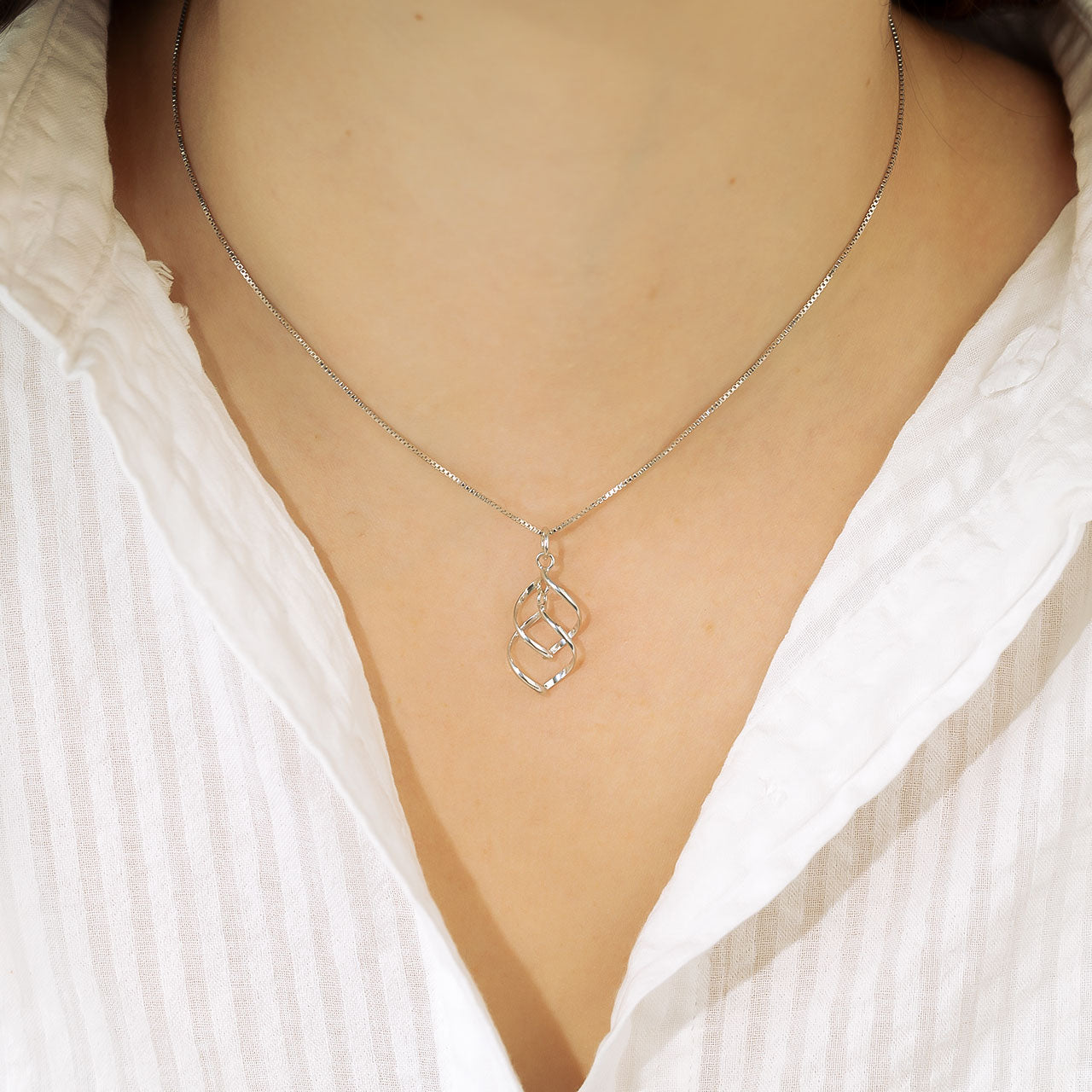Delicate sterling silver pendant featuring intertwined spiral waves suspended from a fine chain, exemplifying elegant and contemporary silver jewellery design.