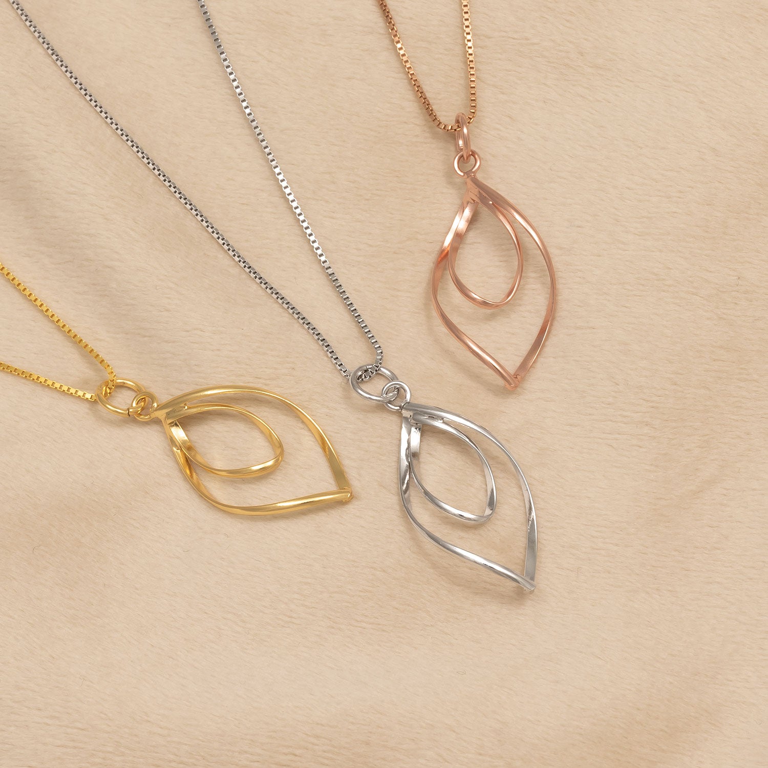 Three sculptural open loop pendant necklaces in yellow gold vermeil, rose gold vermeil, and sterling silver, each suspended from delicate matching chains for an elegant contemporary look.