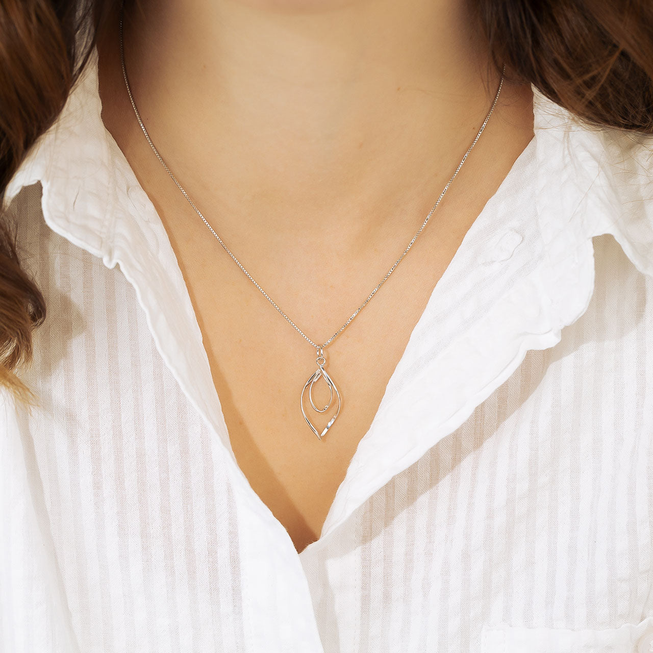 Delicate silver pendant featuring intertwined looping shapes suspended from a fine chain, exemplifying a sculptural and refined sterling silver jewellery design.