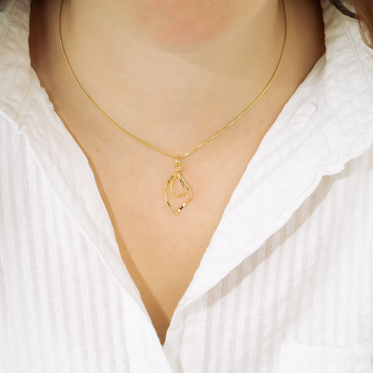 Delicate yellow gold vermeil pendant featuring intertwined fluid loops suspended from a slender chain, combining contemporary elegance with sculptural detail.