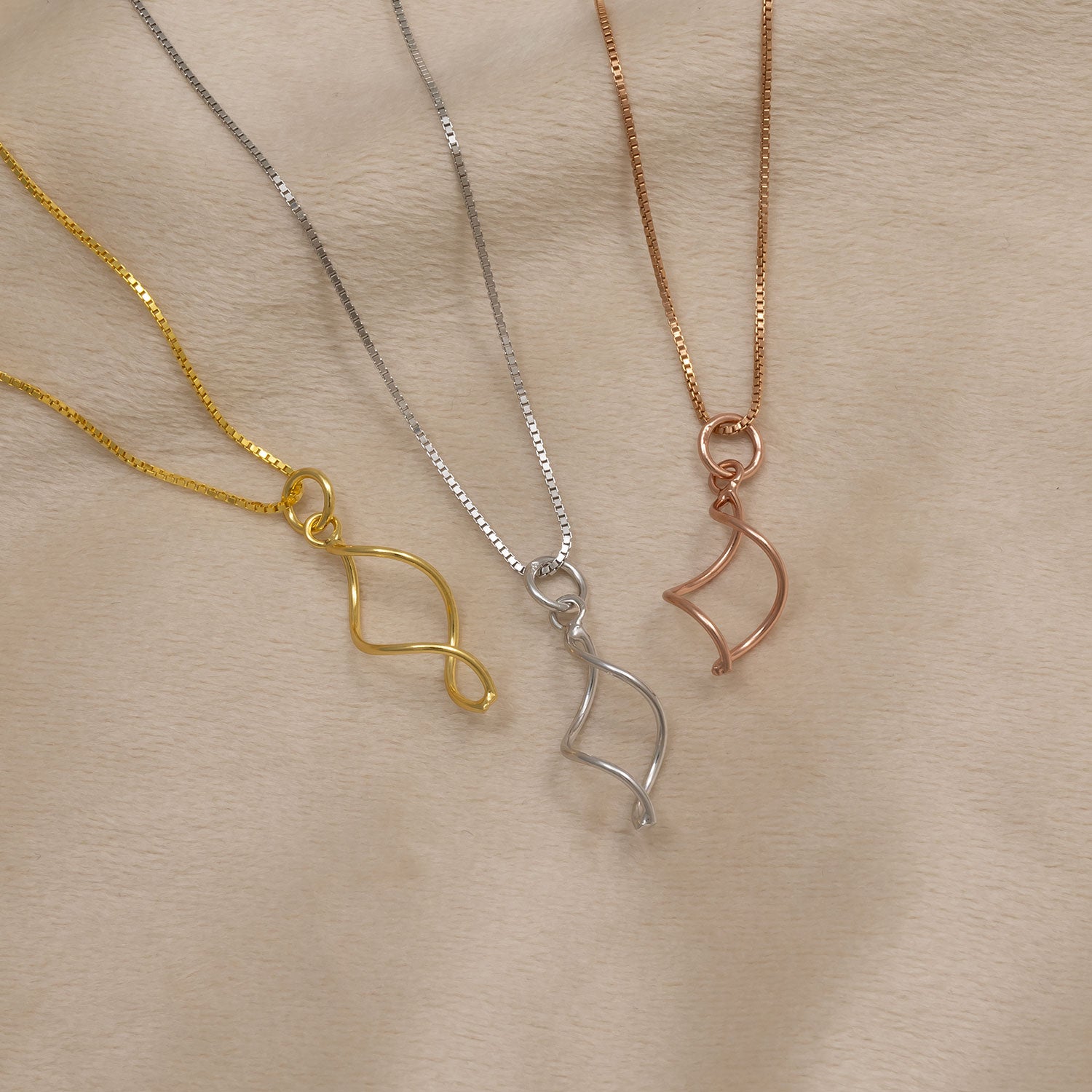 Three delicate necklaces featuring sculptural twisted pendants in yellow gold vermeil, sterling silver, and rose gold vermeil, each hanging from fine chains with a contemporary design.