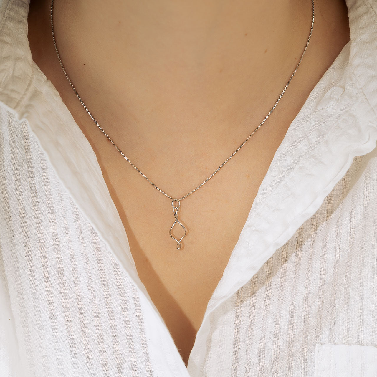 Delicate sterling silver pendant necklace featuring a graceful twist design suspended from a fine chain, exemplifying minimalist and sculptural silver jewellery.