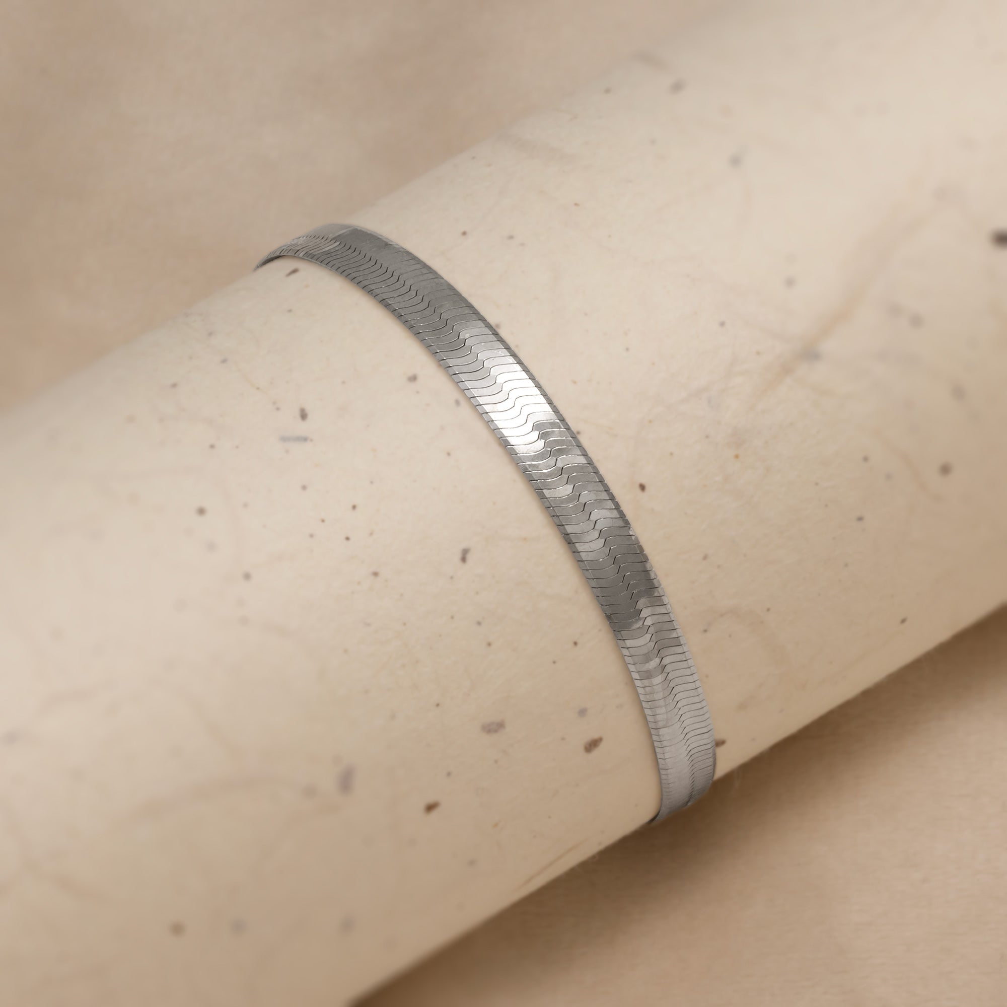 Sterling silver bracelet with a wide herringbone chain design and adjustable extension, showcasing a sleek, contemporary aesthetic in expertly crafted silver jewellery. Placed around a cream tube.