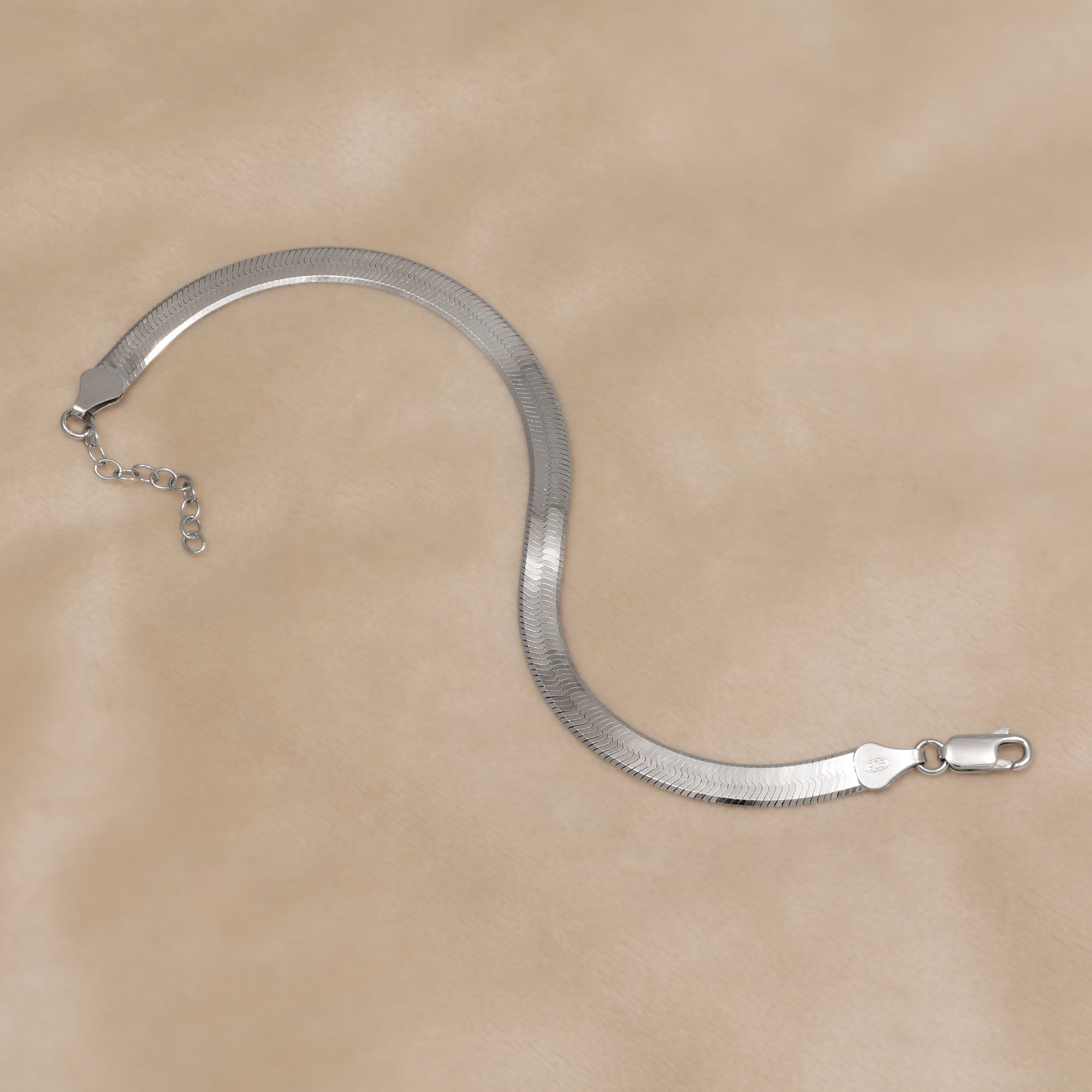 Sterling silver bracelet with a wide herringbone chain design and adjustable extension, showcasing a sleek, contemporary aesthetic in expertly crafted silver jewellery. Placed on a cream velvet cloth.