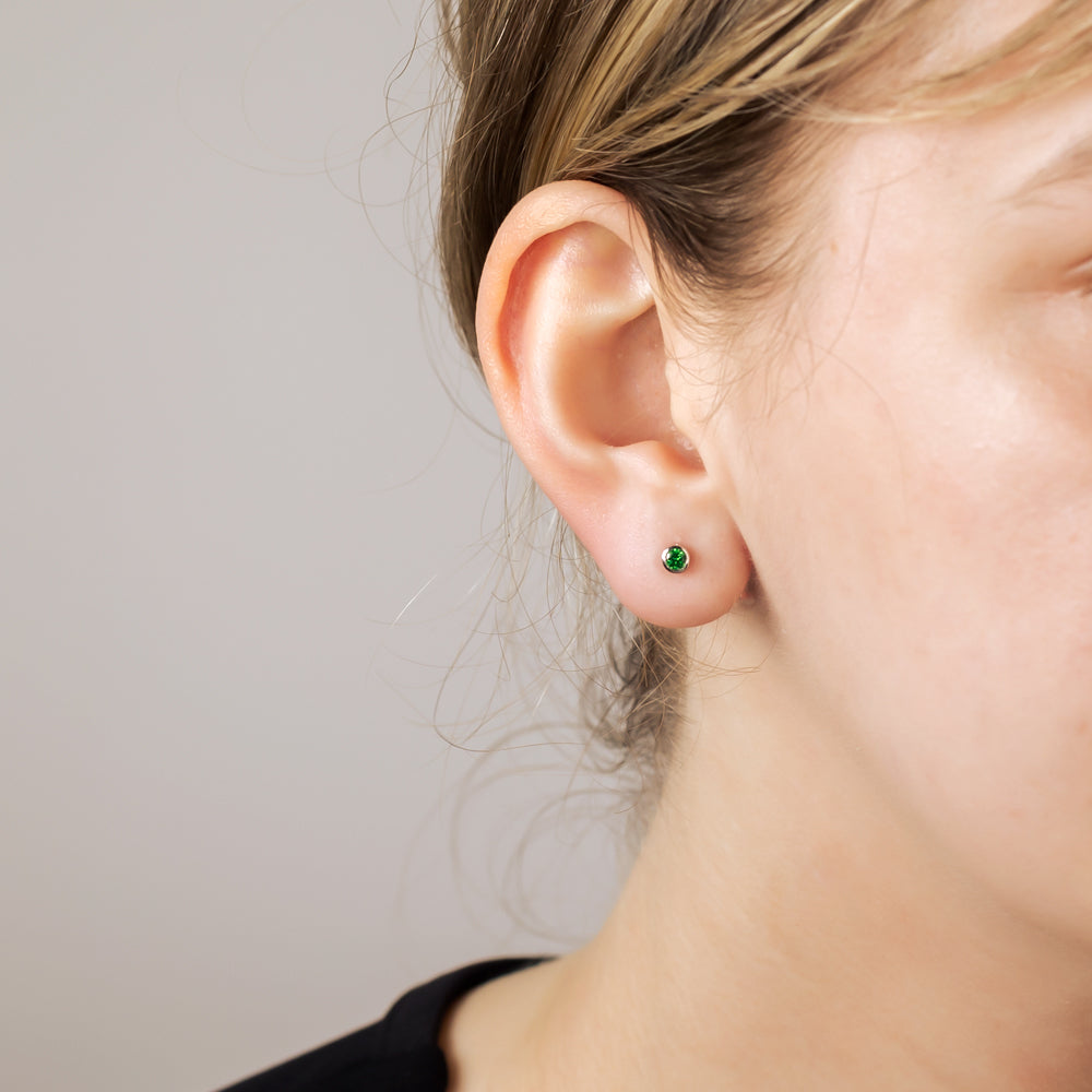 Close-up of a single sterling silver stud earring featuring a brilliant-cut 3mm green stone, worn on the earlobe against a neutral background.