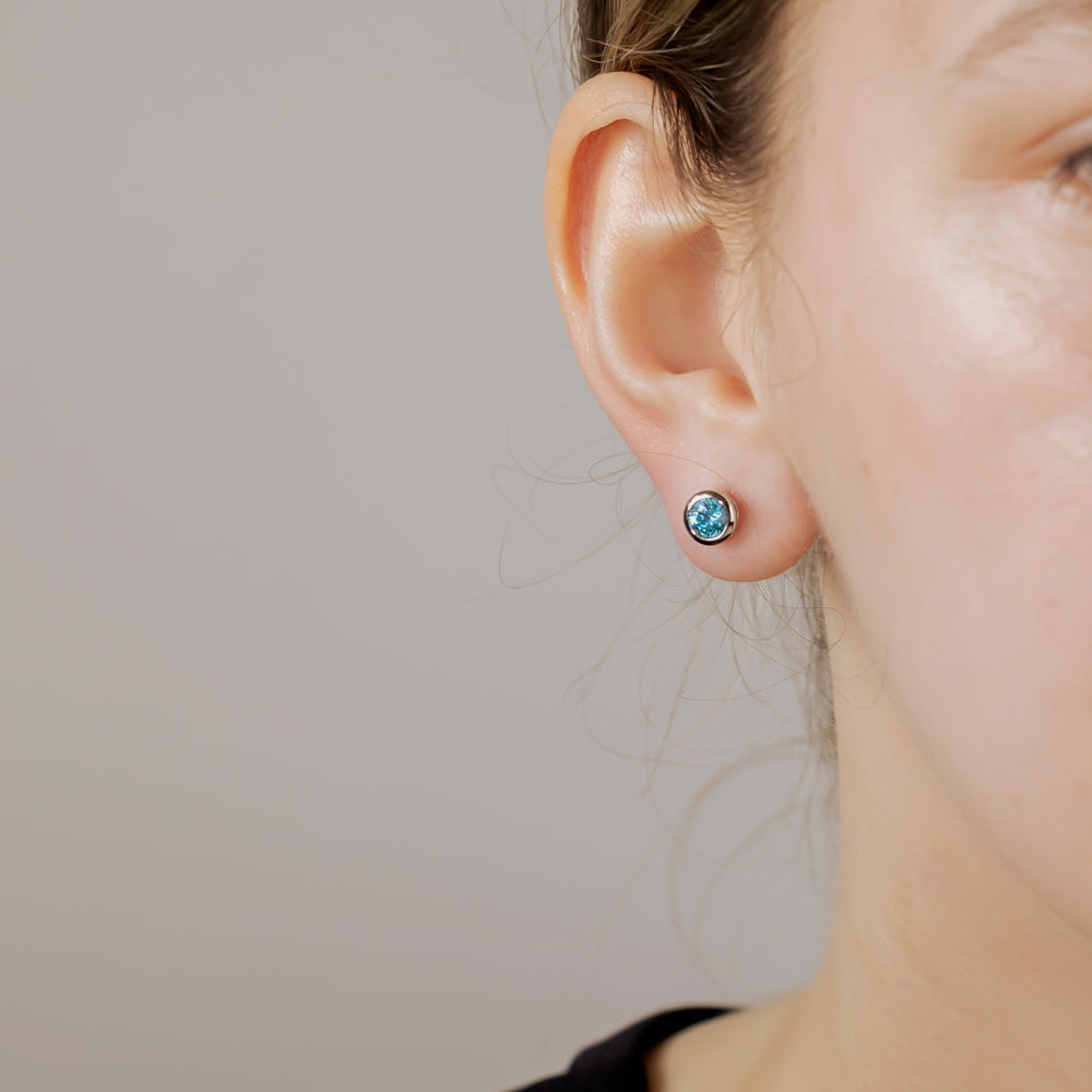 Close-up of a person wearing a sterling silver stud earring set with a brilliant cut aqua stone, highlighting the sleek, contemporary design of the silver jewellery.