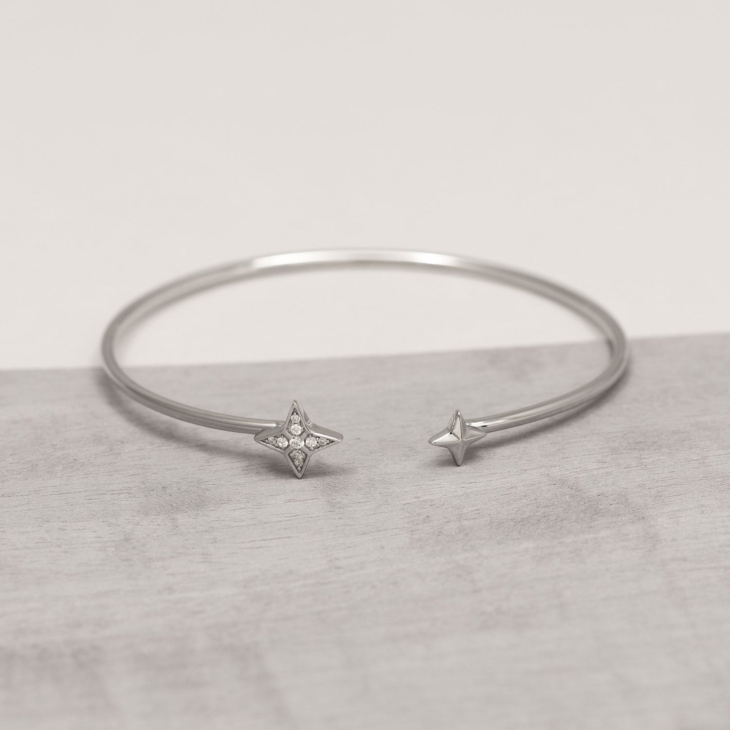 Sterling silver flexi cuff bangle featuring a minimalist open design with star-shaped end caps, one adorned with small sparkling gemstones for subtle elegance.