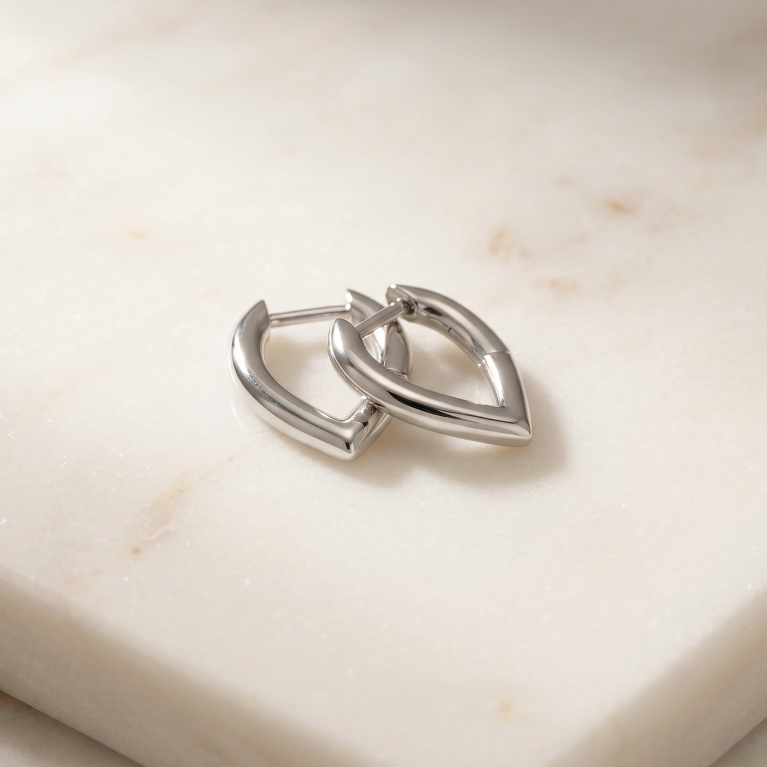 Pair of sculptural sterling silver hinged hoop earrings in a V-shaped design, laid on a marble background.