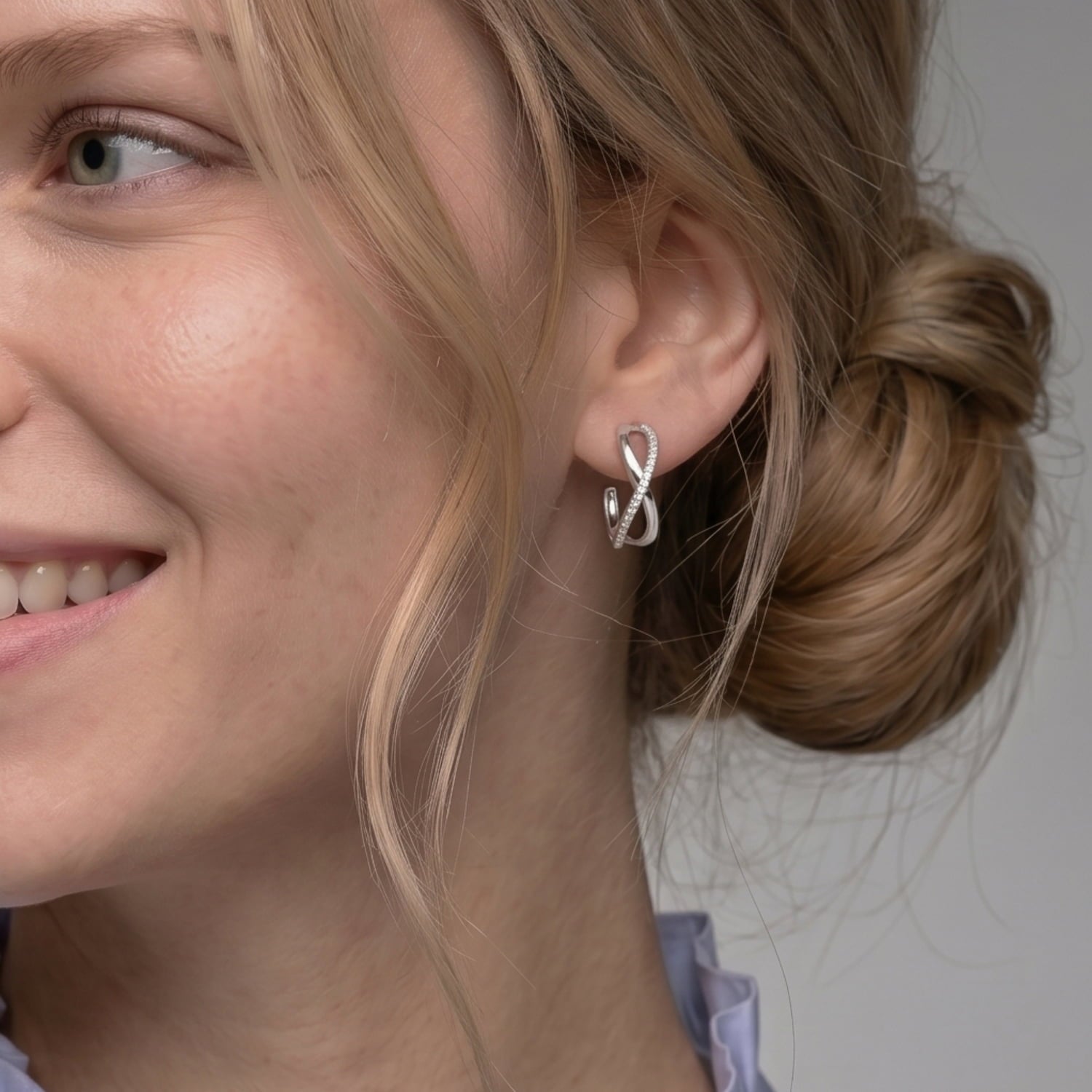 Model wears pair of large sterling silver hoop earrings featuring an elegant crossover wave design accented with pavé-set stones
