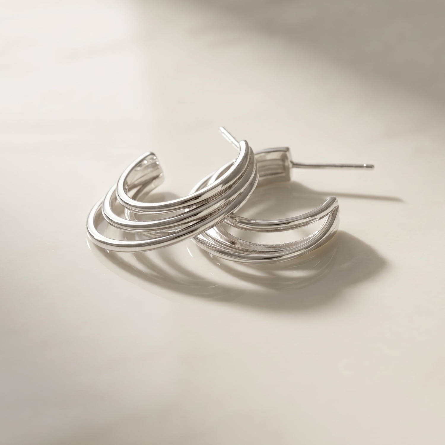 Pair of sterling silver hoop earrings featuring a sculptural four-strand design with a polished finish, laid upon a marble background