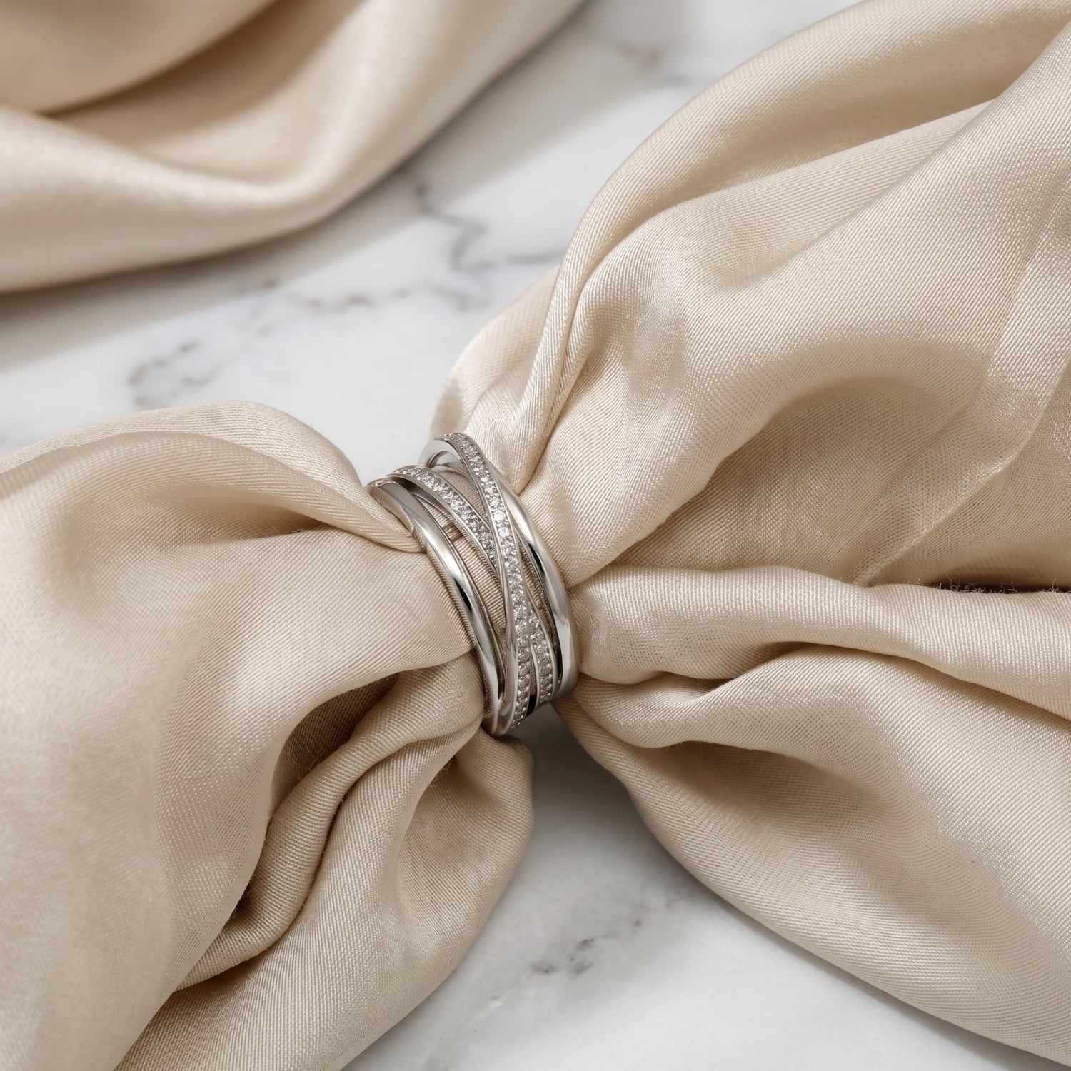 Multi-stranded sterling silver ring, with two strands of pricision-set sparking cubic zirconia stones. The ring is place on ivory silk against a marble background.