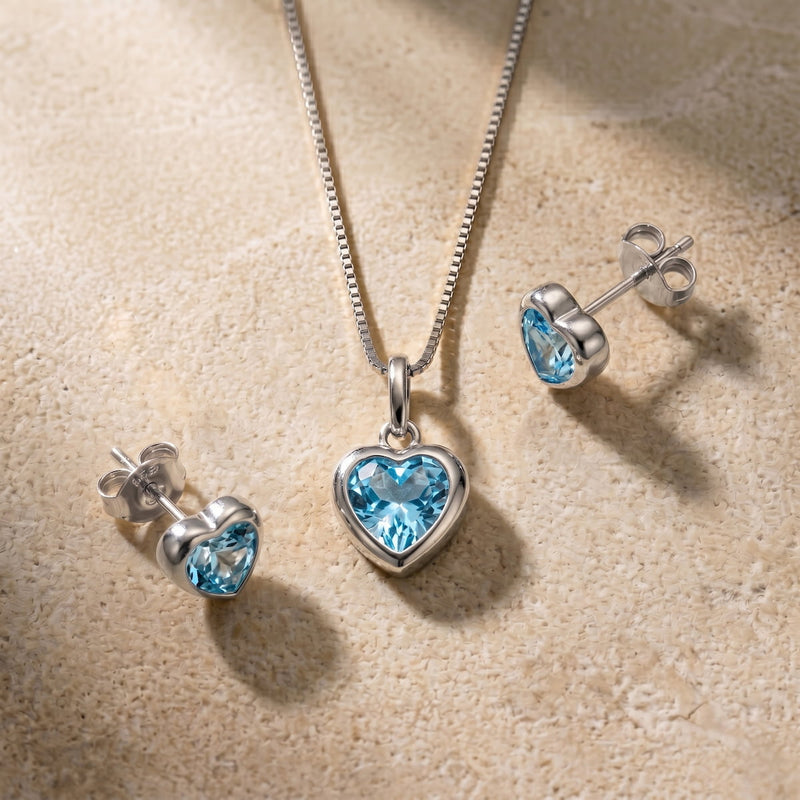 Silver jewelry set with heart-shaped blue topaz gemstones on a beige surface