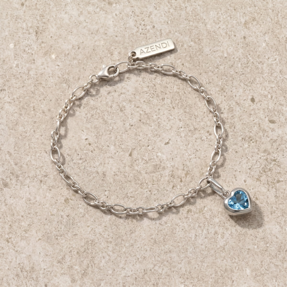 Sterling silver bracelet with a heart-shaped blue topaz gemstone on a beige limestone surface