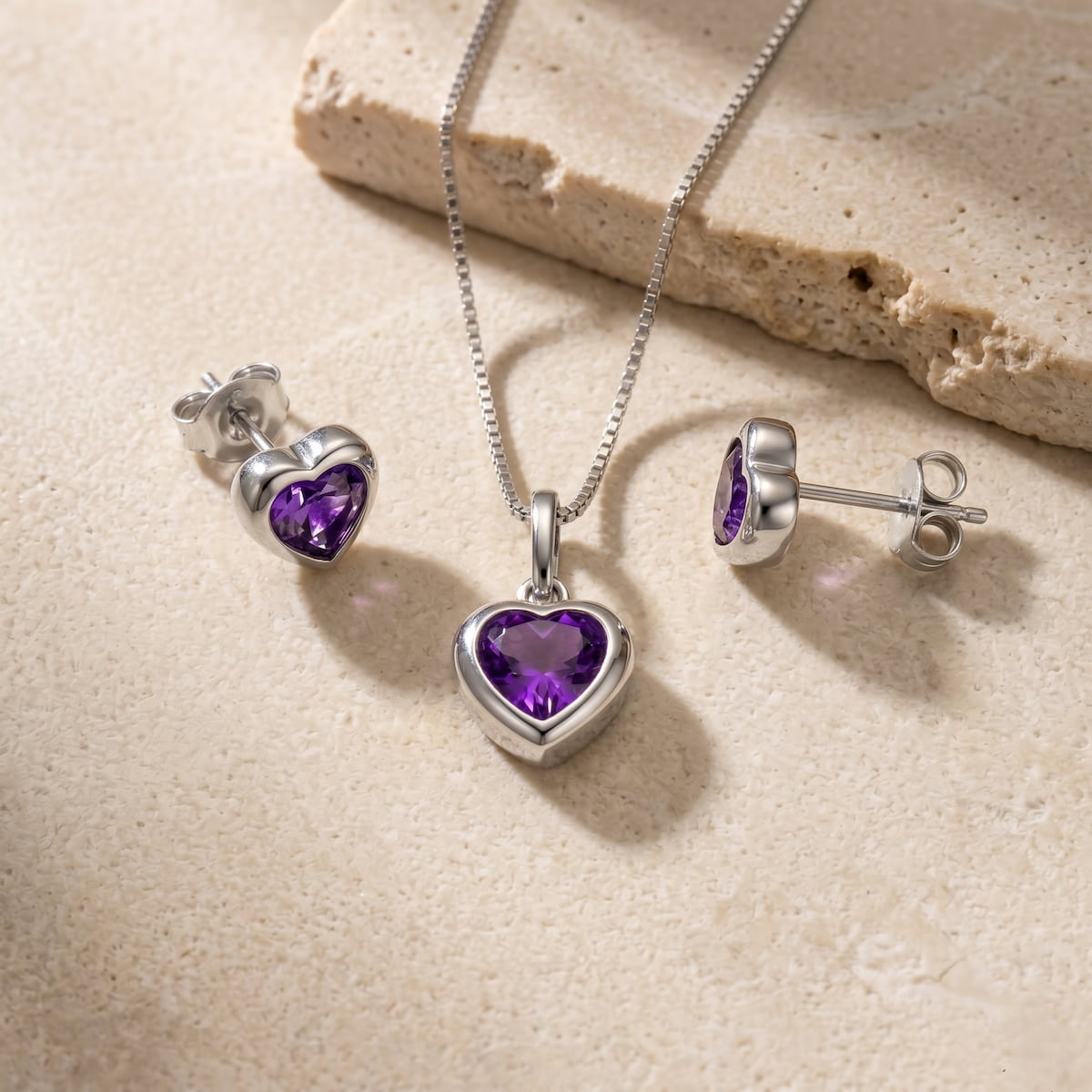 Silver heart-shaped jewellery set with amethyst stones on a beige stone surface