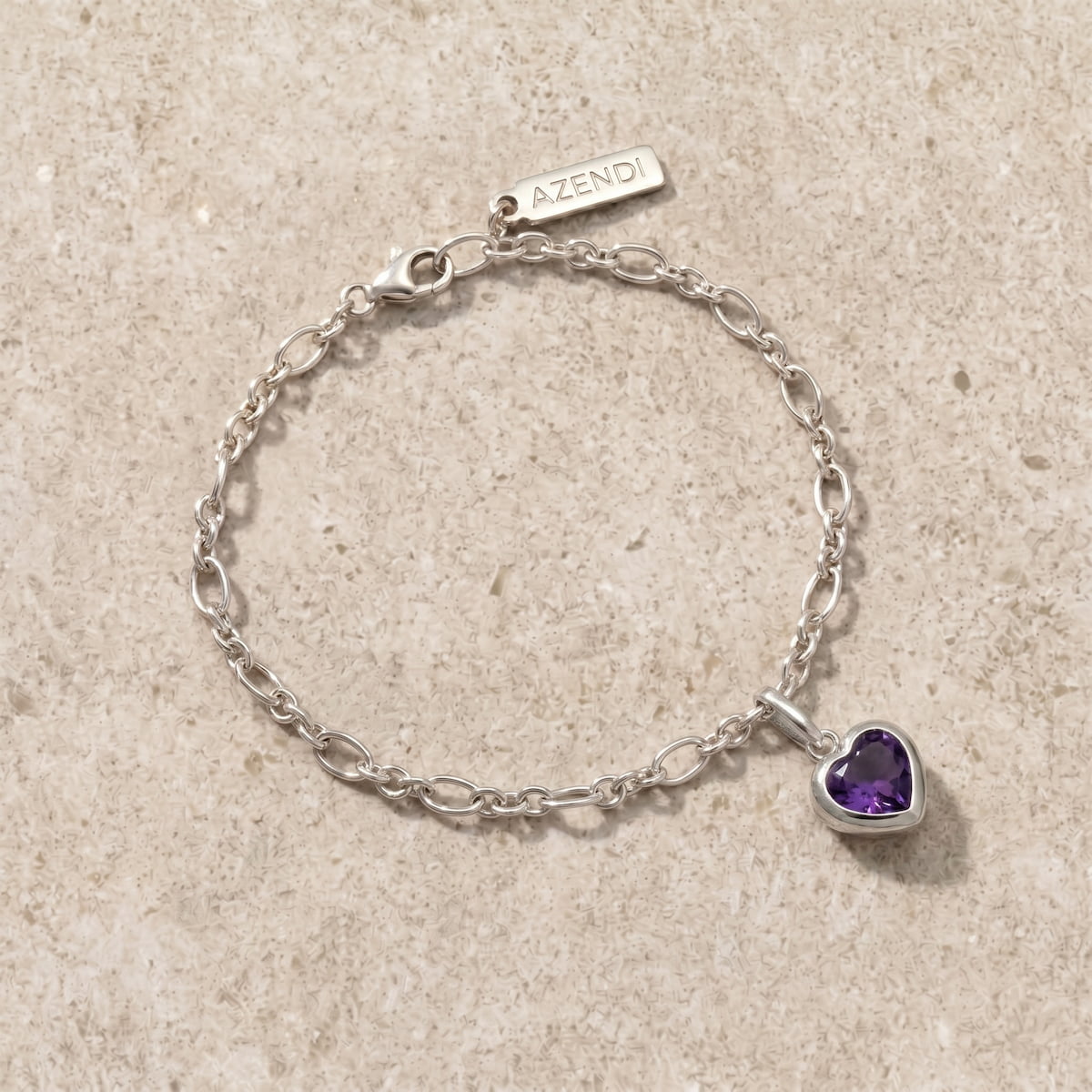 Silver bracelet with a purple amethyst heart charm on a beige limestone surface