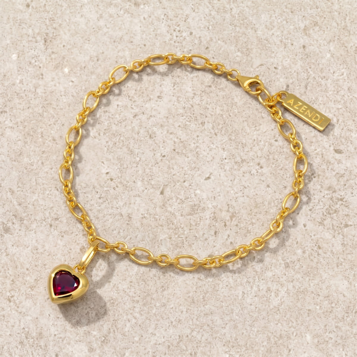 Gold vermeil bracelet with a heart-shaped garnet charm on a limestone surface