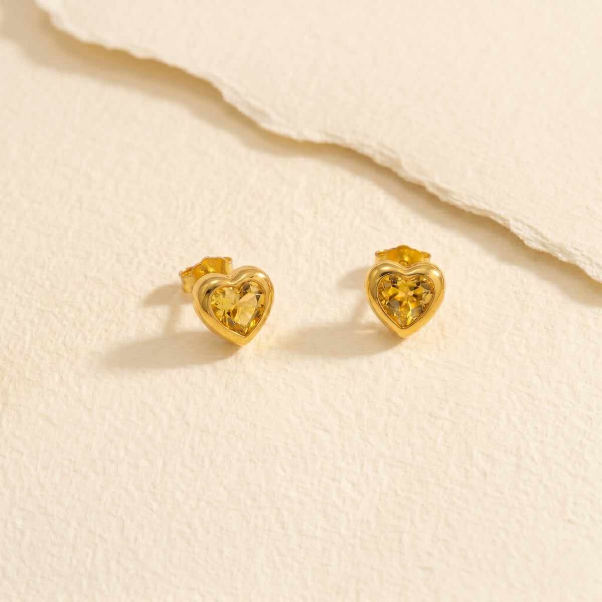Heart-shaped gold vermeil earrings with citrene emstones on a paper background