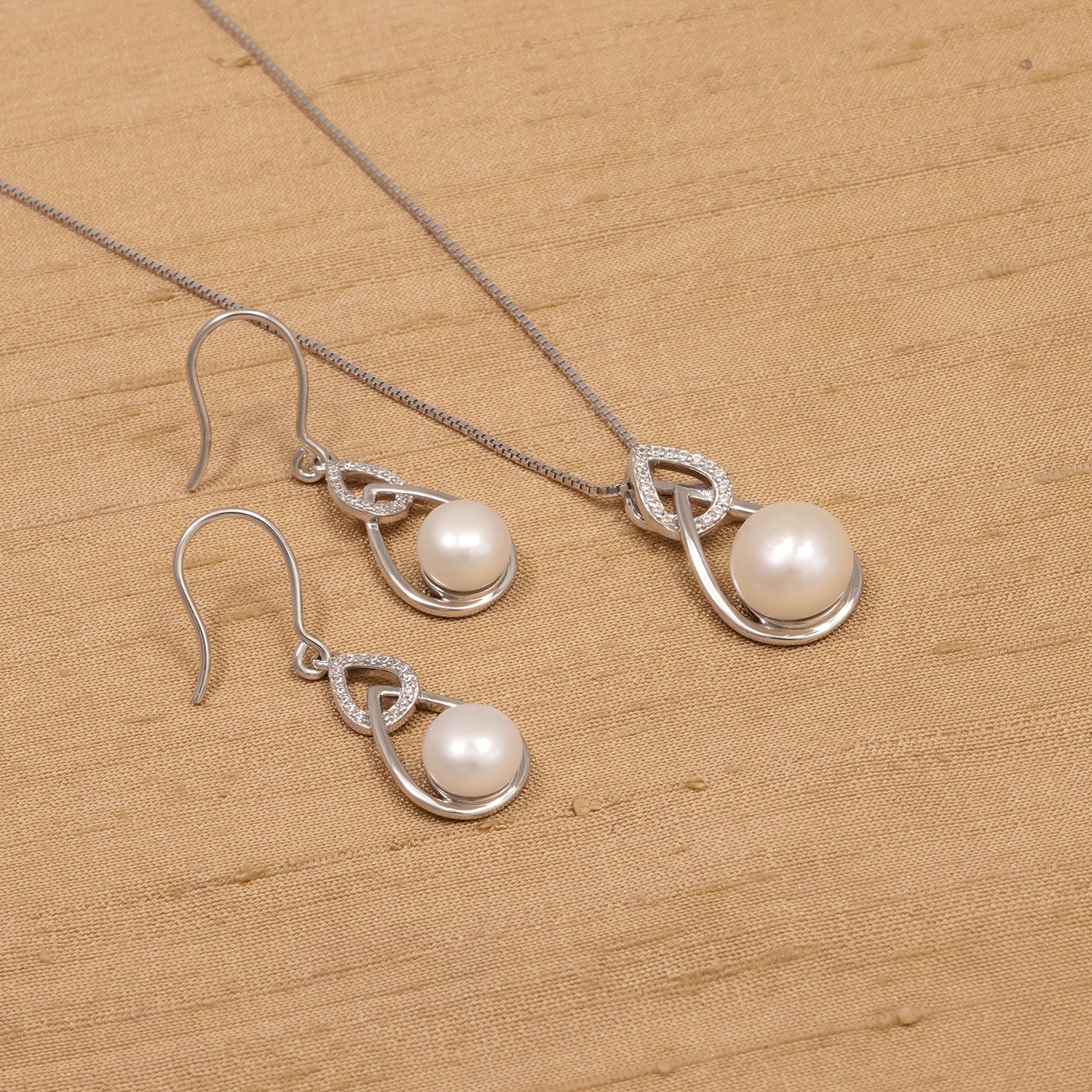 Pair of sterling silver drop earrings with teardrop-shaped frames featuring freshwater pearls and small sparkling accents, styled alongside a matching pendant necklace.