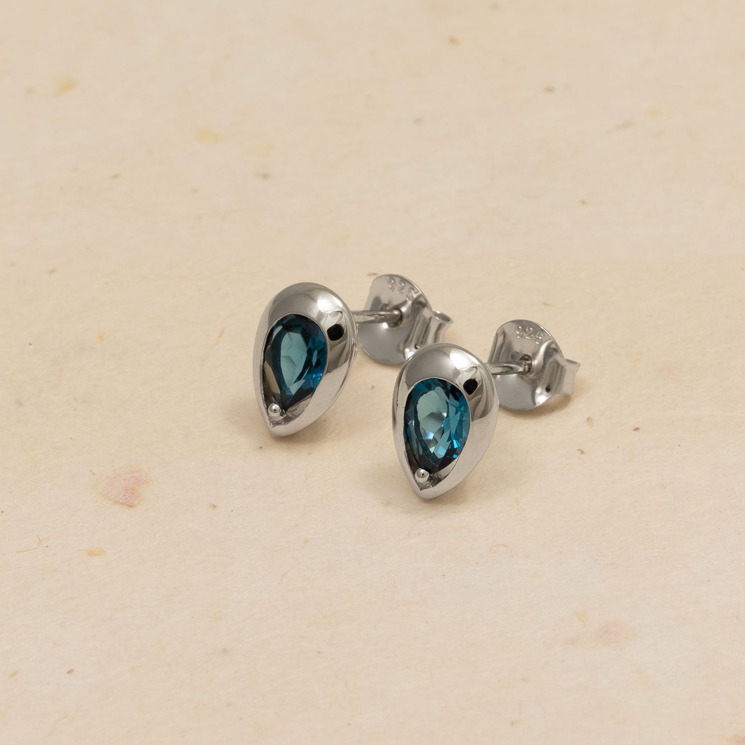 Pair of polished sterling silver stud earrings set with deep blue London Blue Topaz stones in a teardrop shape, highlighting a refined and modern silhouette.