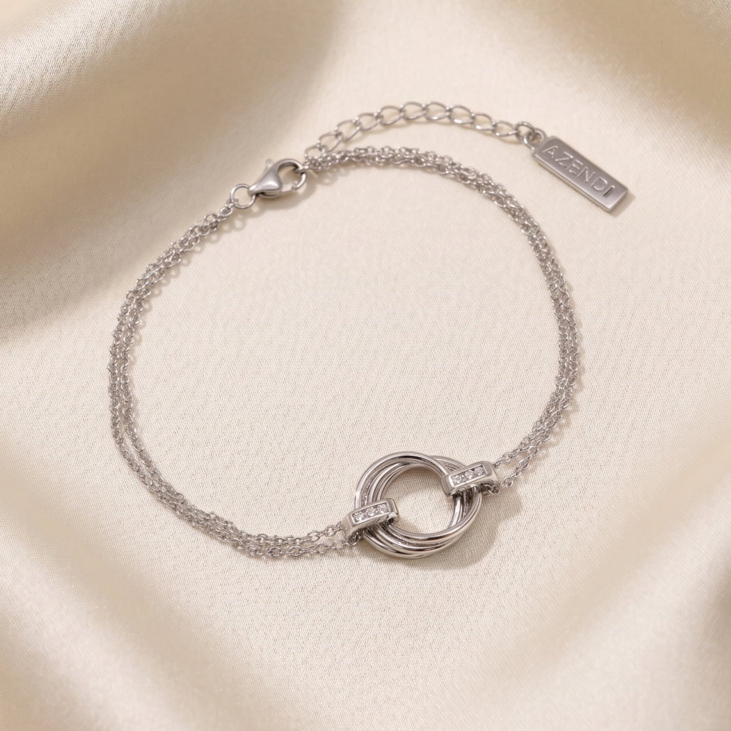 An adjustable sterling silver bracelet featuring an intertwined love knot centerpiece accented with lab-grown diamonds, crafted for refined contemporary elegance, laid on a cream silk backdrop.