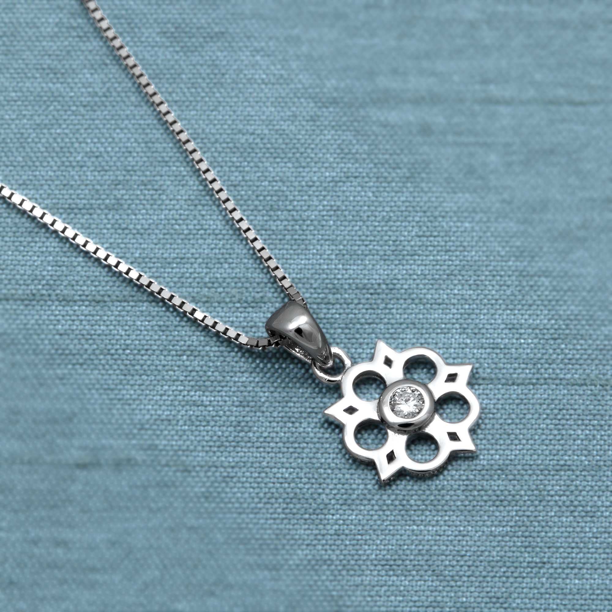 Sterling silver Yorkshire rose pendant featuring a 0.07 carat lab-grown diamond at the centre, suspended on a delicate fine chain with sculptural elegance. Placed on a teal satin cloth.