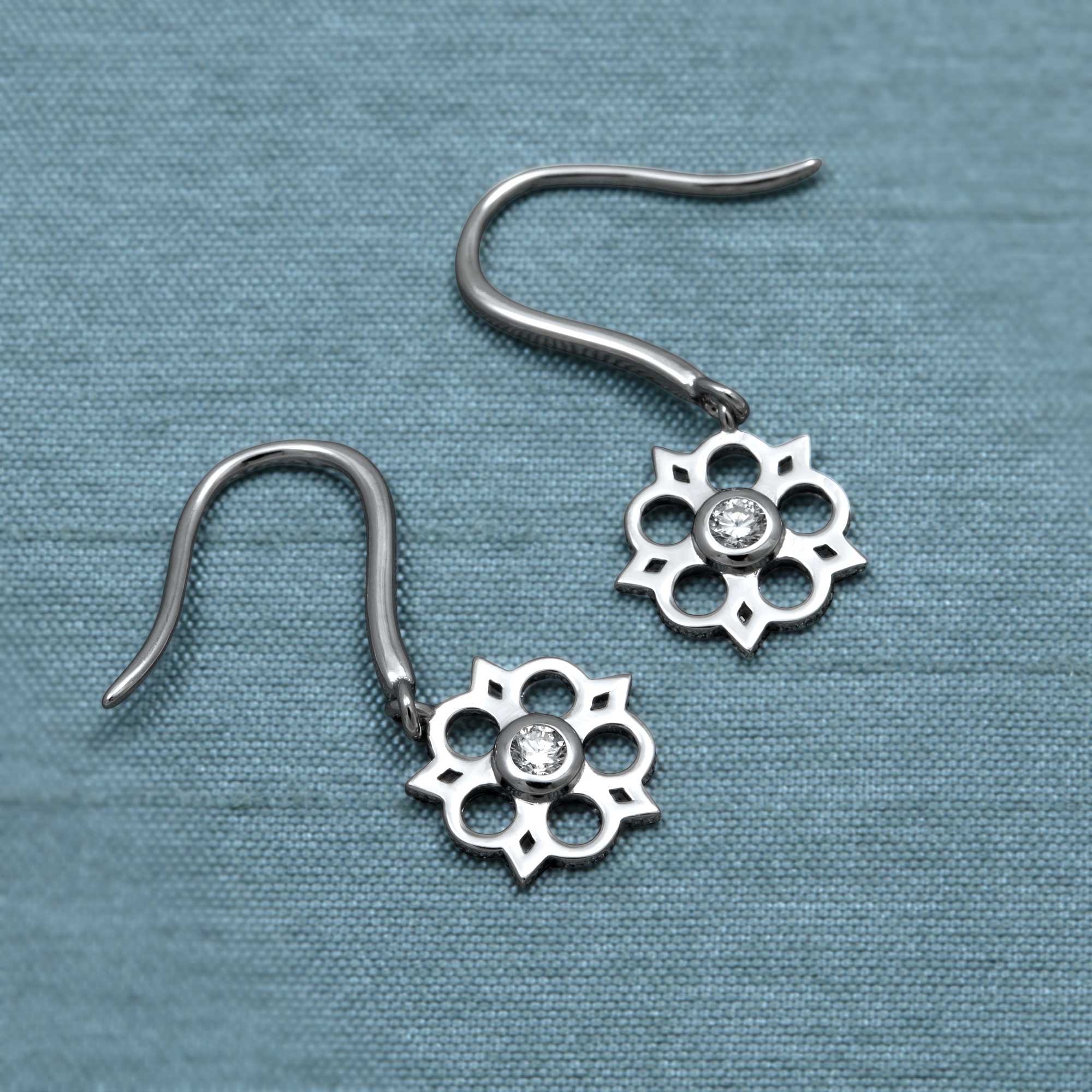 Delicate sterling silver drop earrings featuring an openwork Yorkshire rose motif with a central lab-grown diamond. Place on a teal satin cloth.