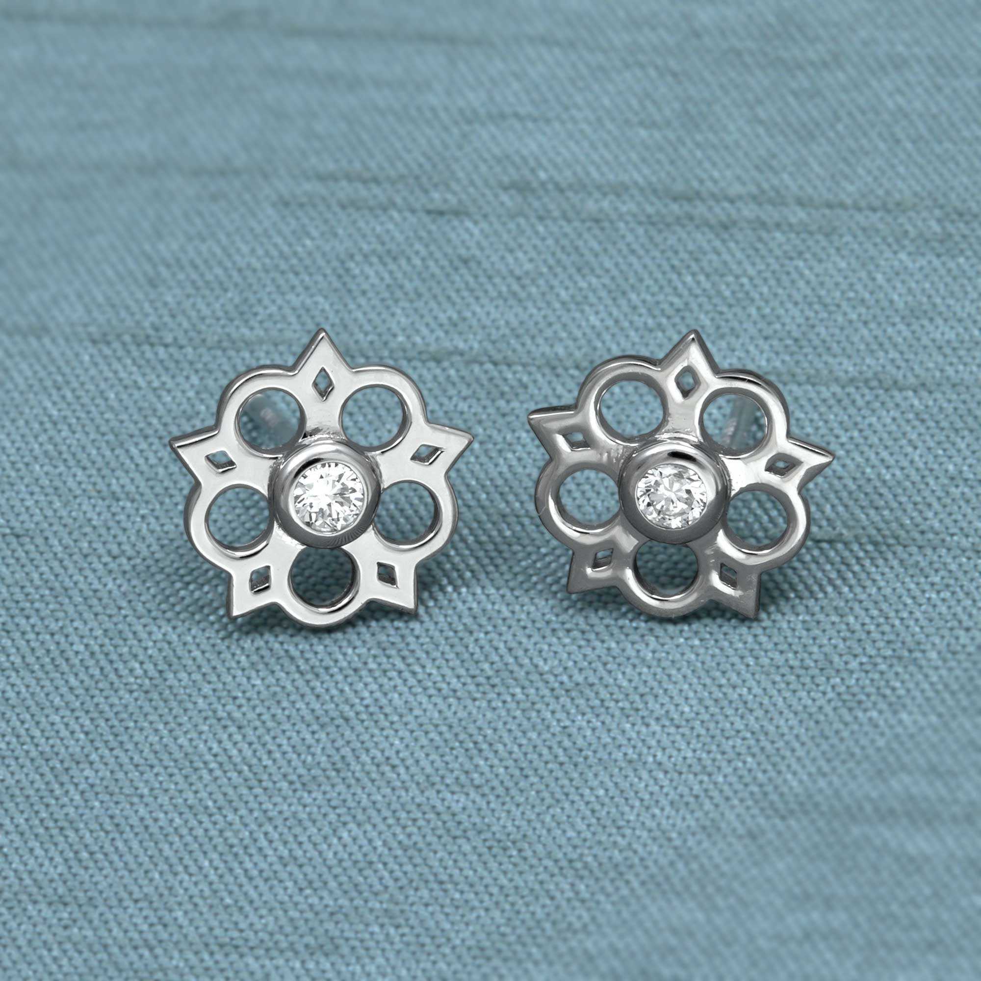 Delicate sterling silver stud earrings featuring an openwork Yorkshire rose motif with a central lab-grown diamond, combining elegant floral design with contemporary silver jewellery. Placed on a teal satin cloth.