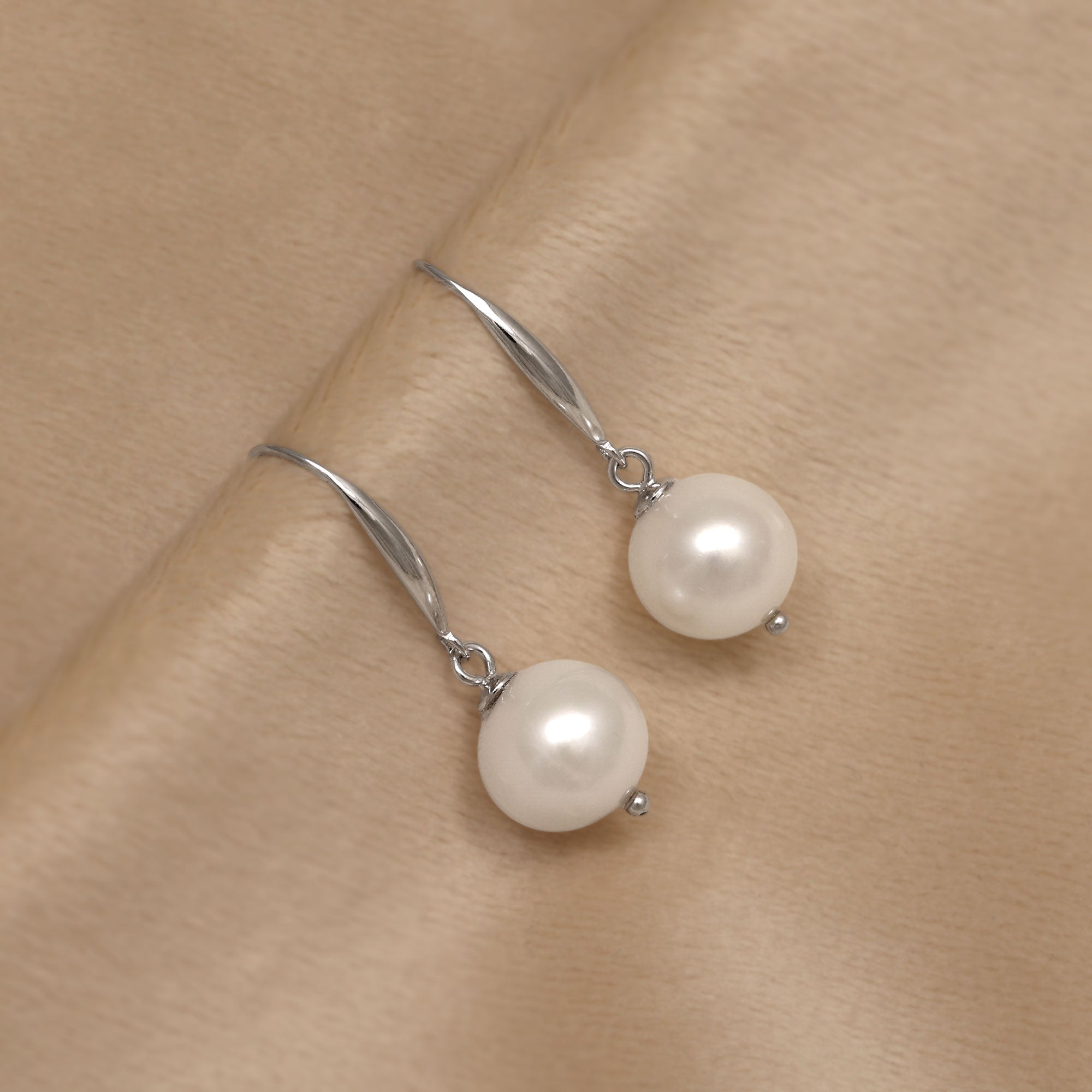 Pair of white spherical freshwater pearl earrings on a cream background