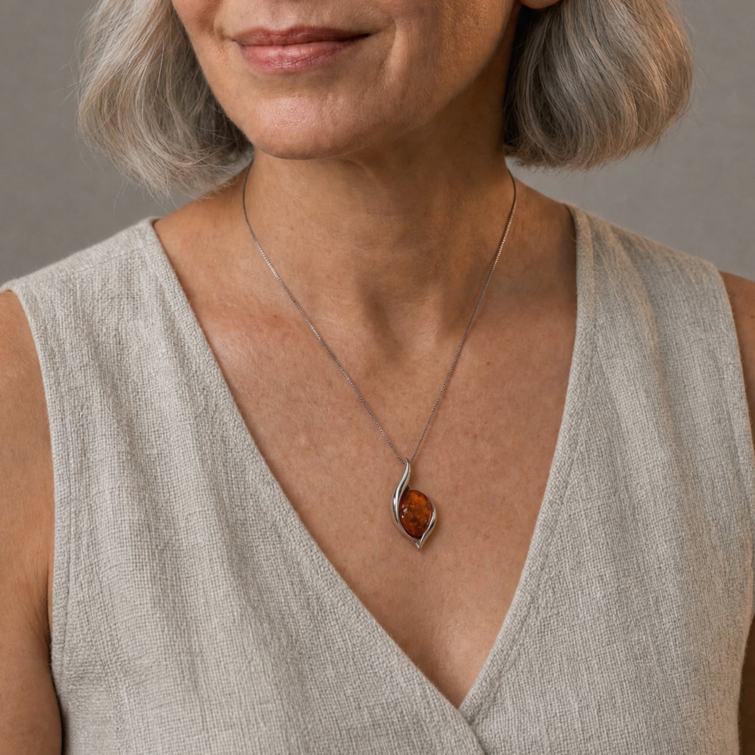 A close-up of a woman wearing a silver pendant necklace with a teardrop-shaped amber stone, paired with a beige linen top.
