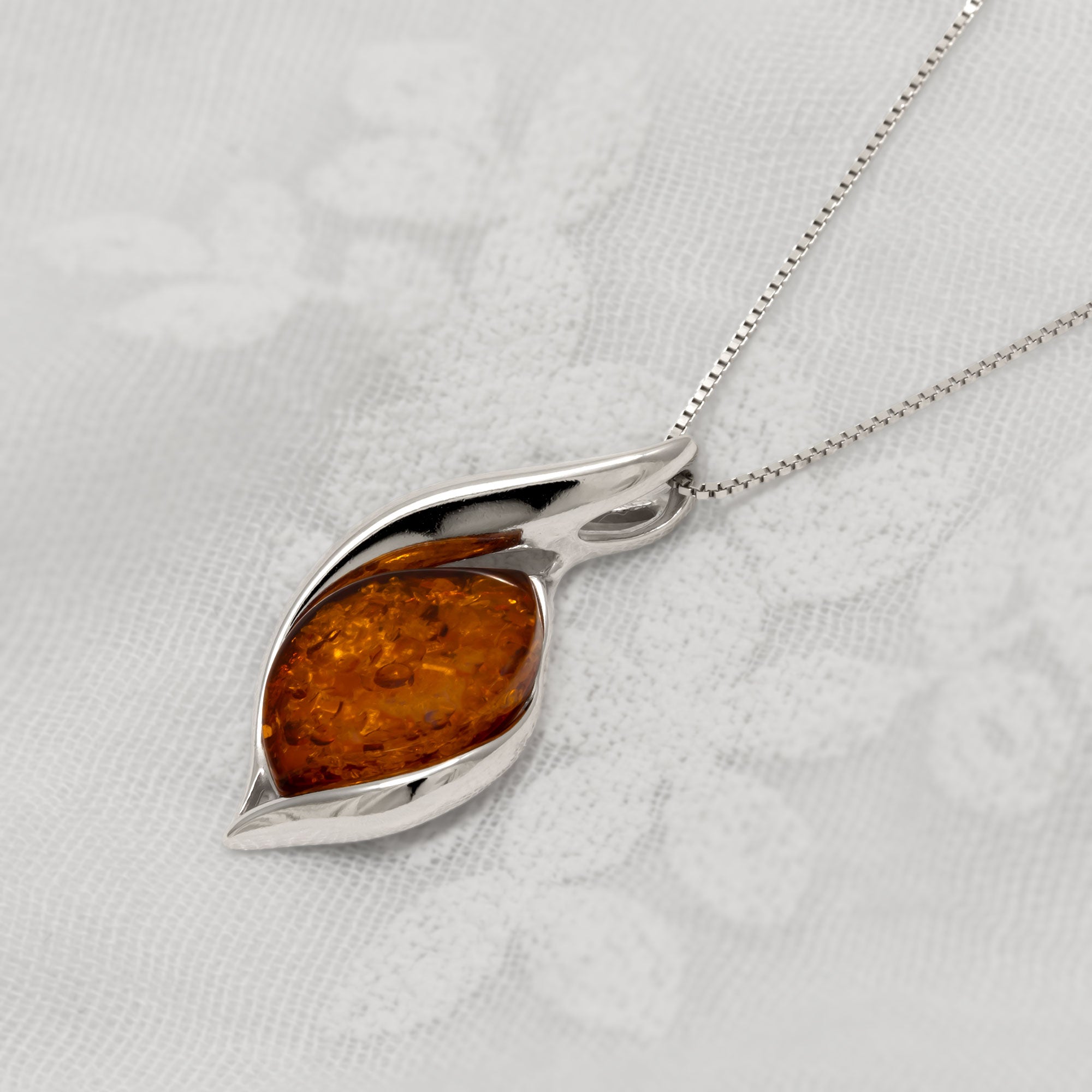 Silver pendant with amber stone on a white fabric background