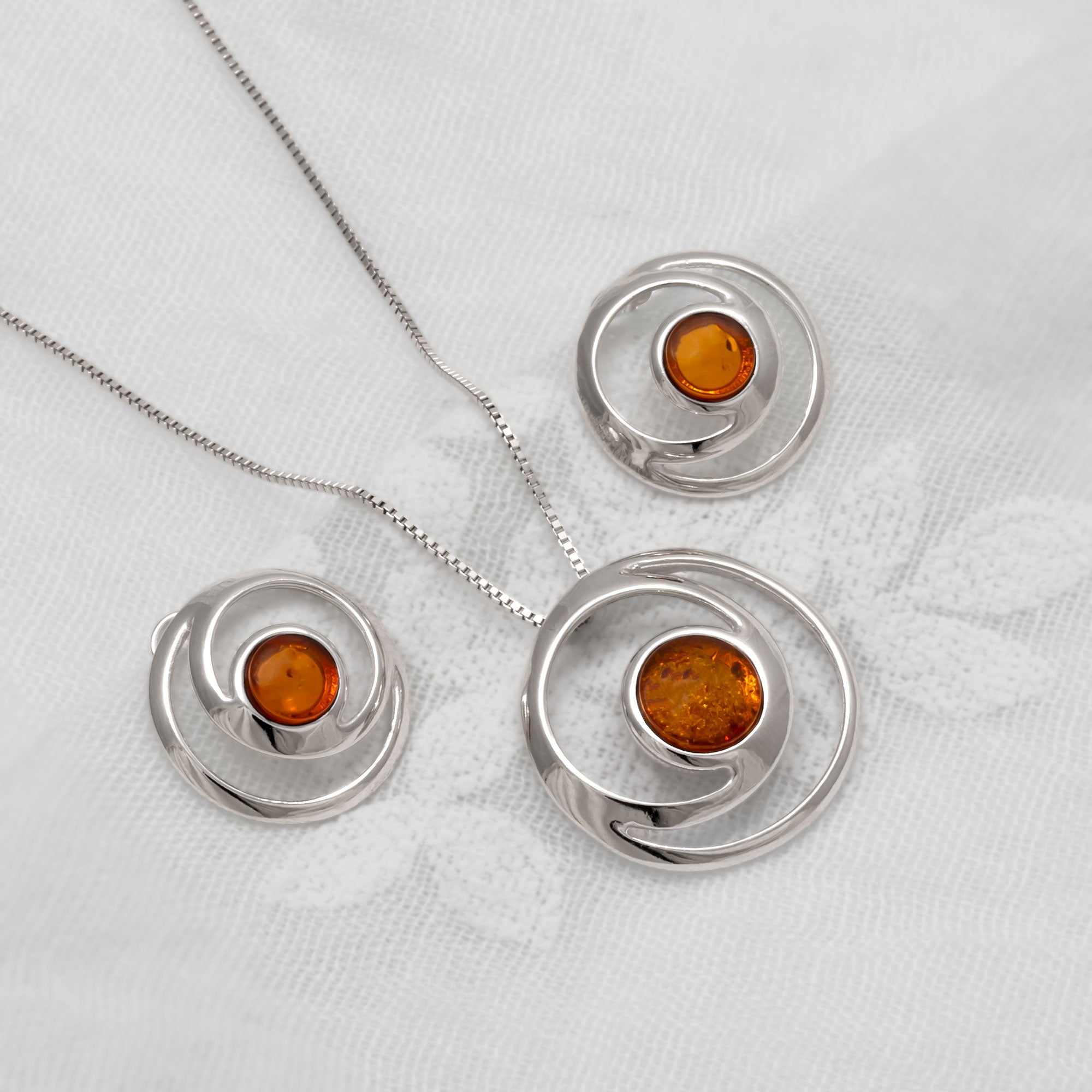 Silver jewellery set with amber gemstones on a white fabric background