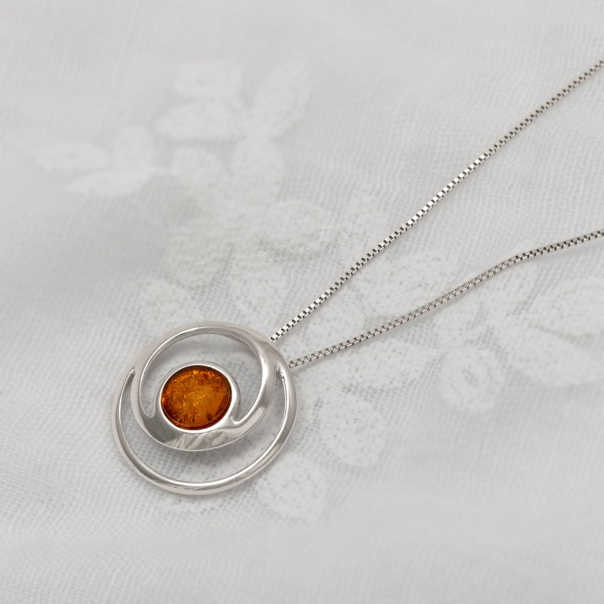 Silver necklace with a round pendant featuring an amber gemstone on a light grey background